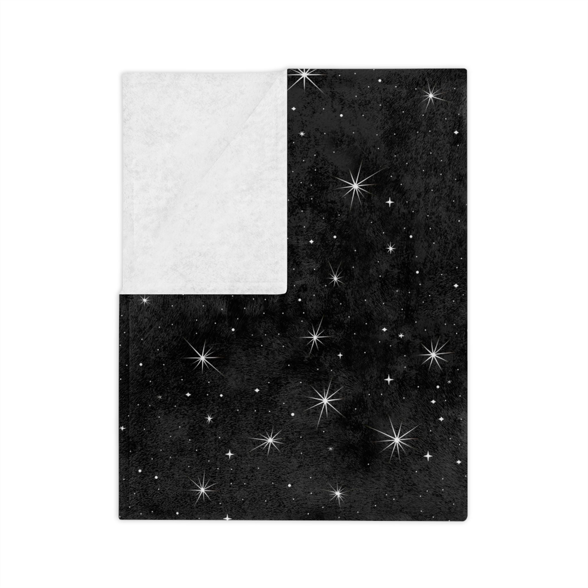 Folded black starry throw blanket with celestial night sky print on soft velveteen.