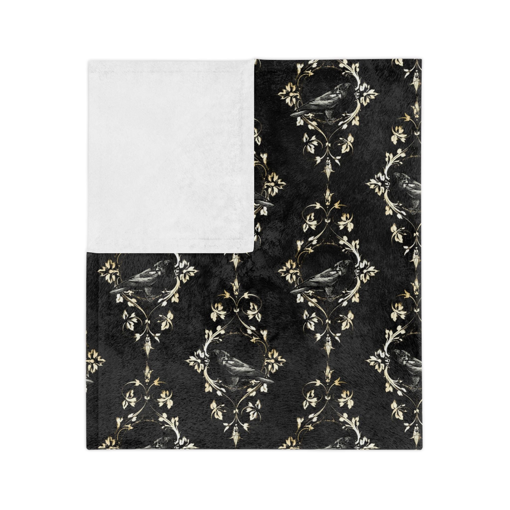 Folded black raven blanket with ornate Victorian Gothic motif on a dark background with white backside.