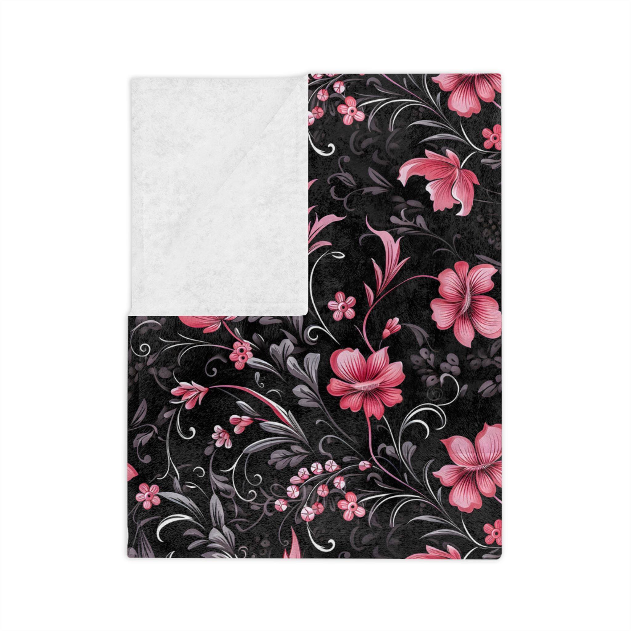 A moody, dark floral throw blanket folded showing the white underside and velveteen material.