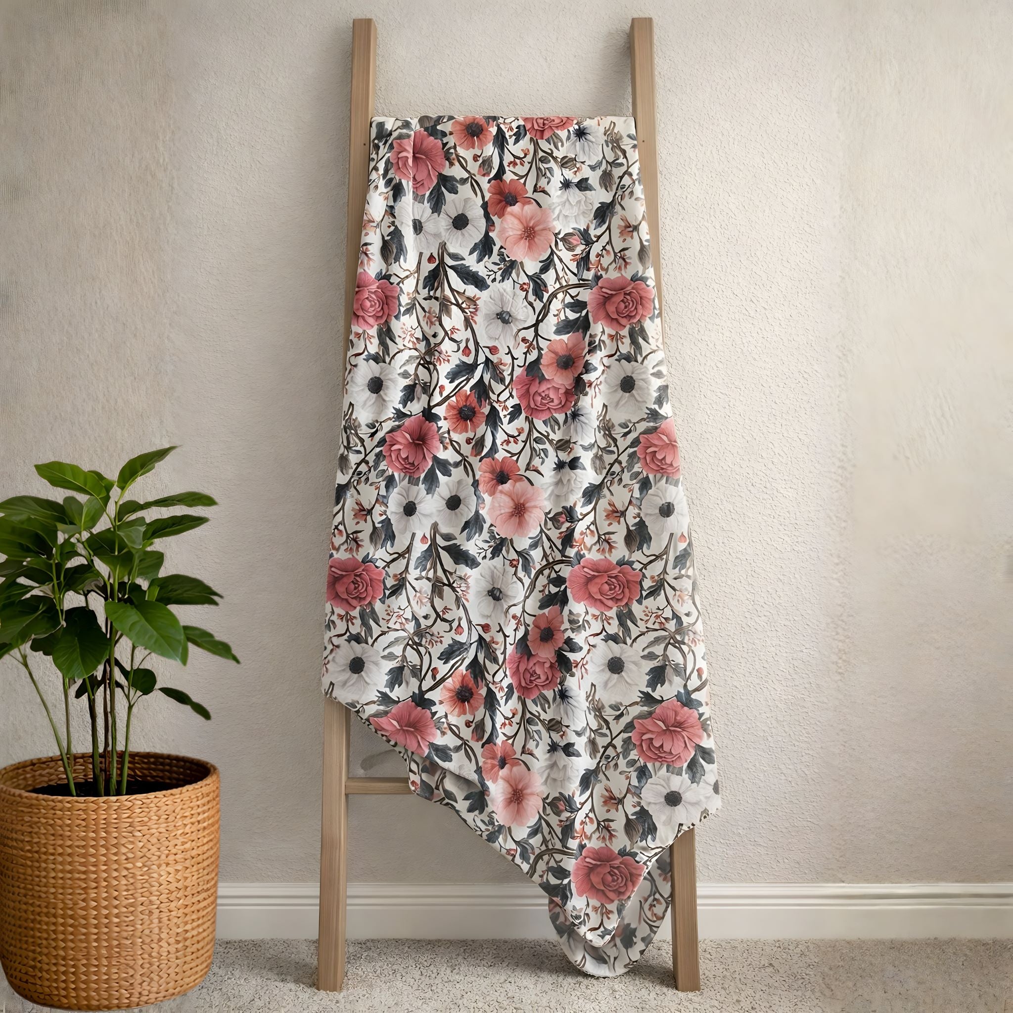 Floral-patterned blanket draped over a wooden ladder against a neutral wall with a plant beside it.