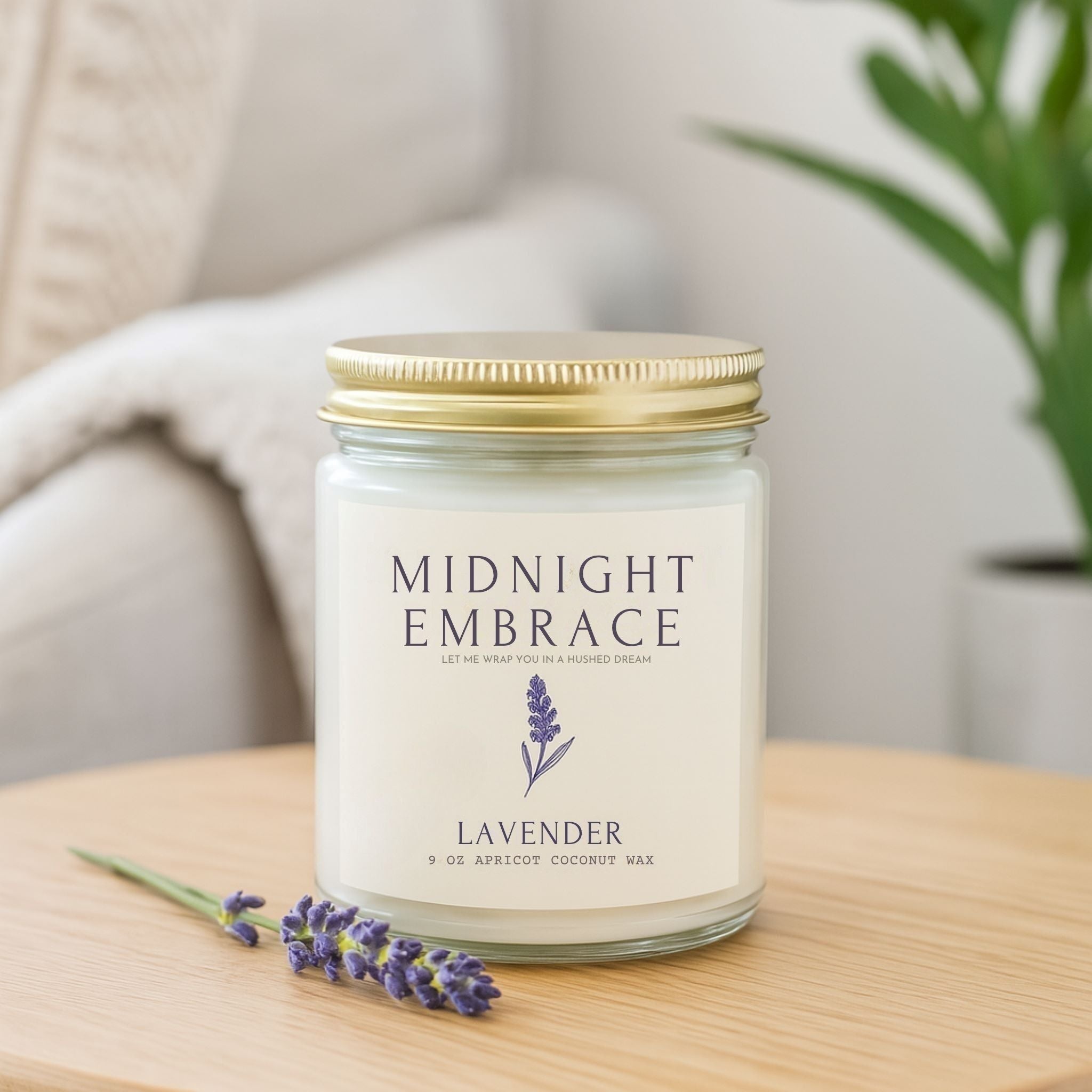 9 oz Lavender scented candle in a clear glass jar with gold lid on a table with couch behind it.