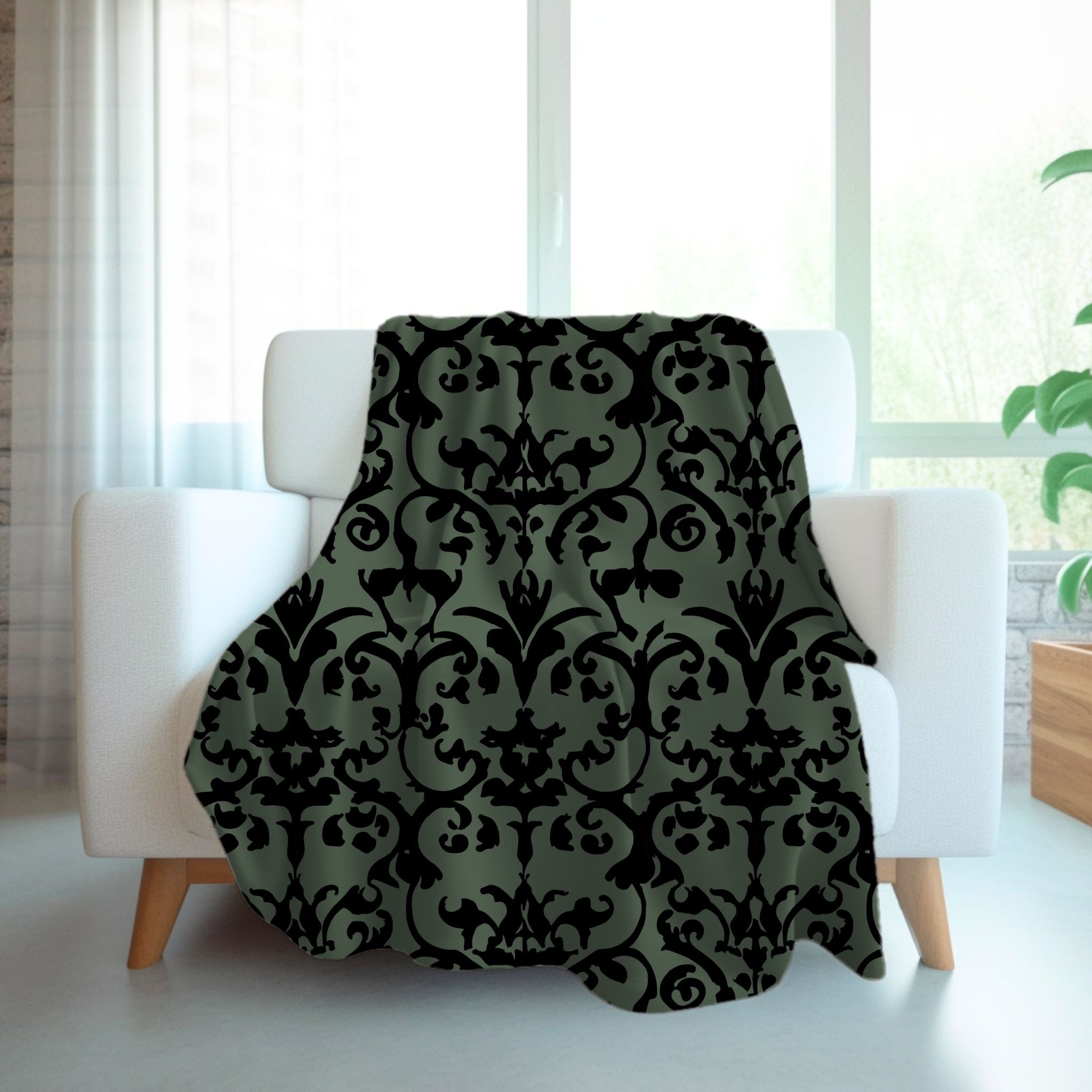 A gothic style throw blanket with a damask pattern in sage green and black displayed on a clothing rack, in a room with decor.