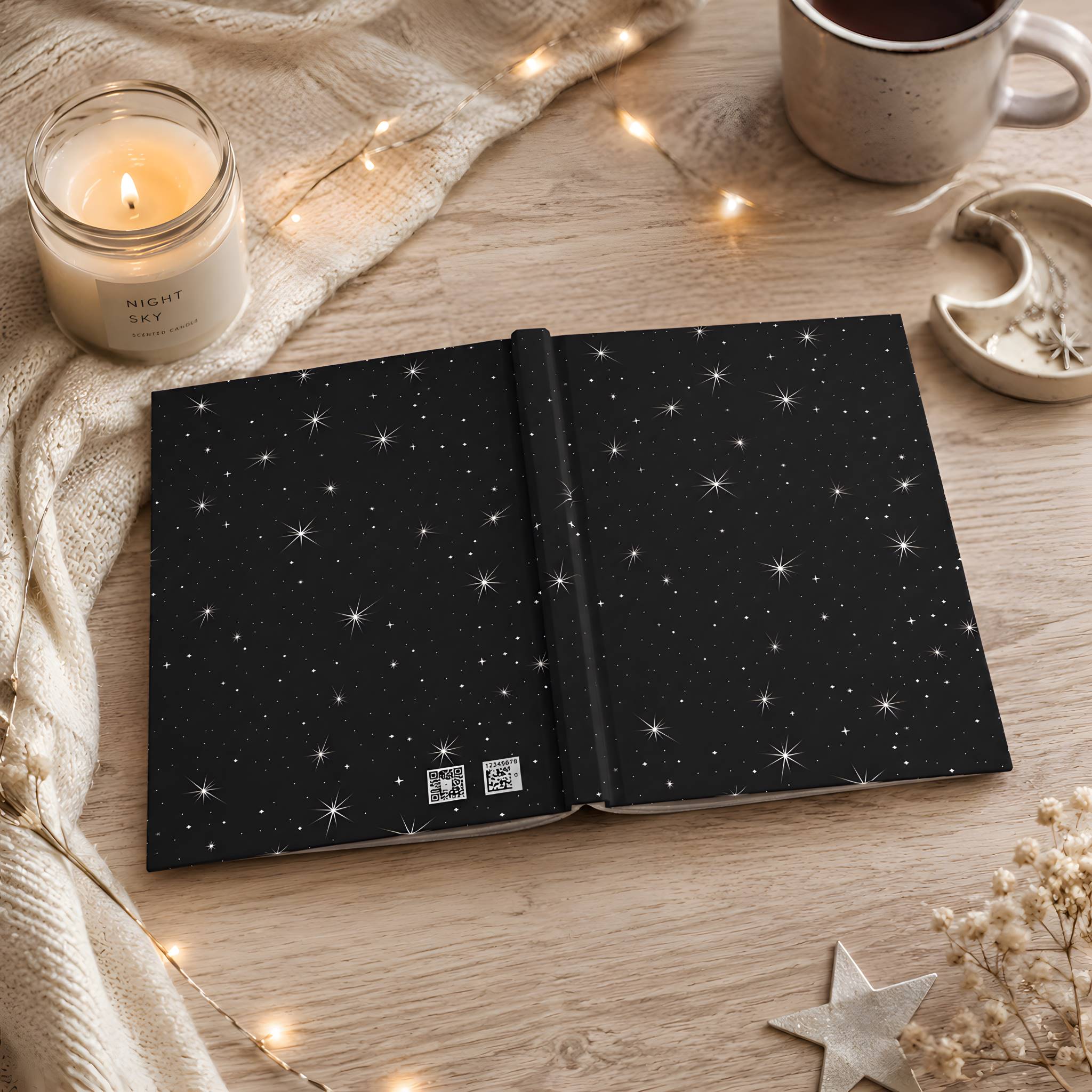 Open hardcover journal with star pattern on a wooden surface with a candle and mug.
