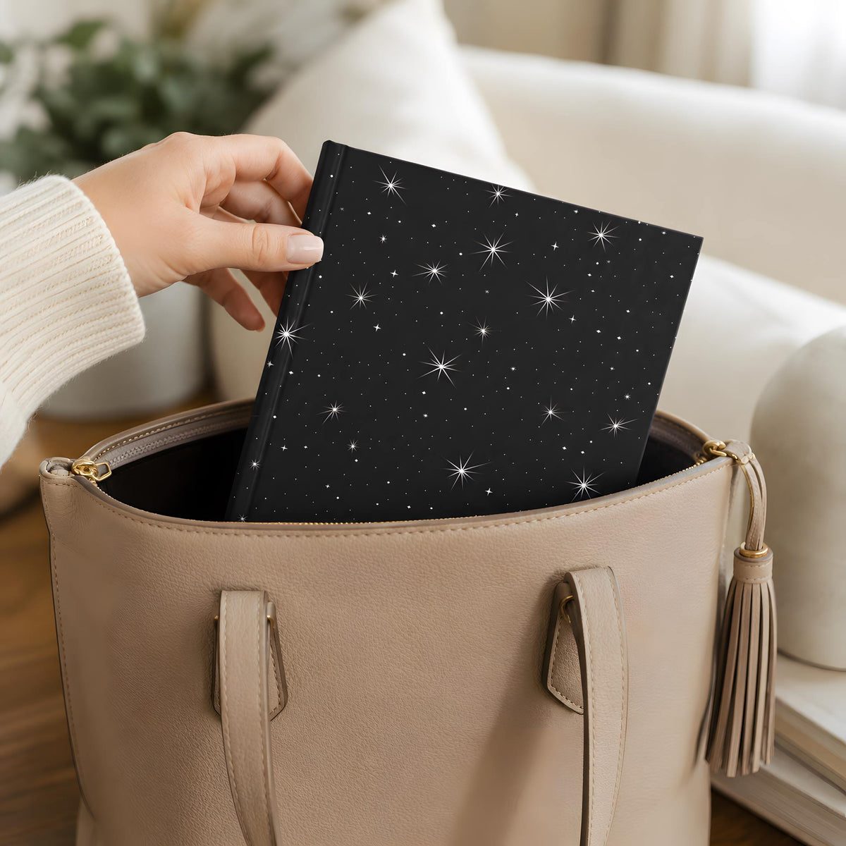 Hand placing a whimsigoth celestial journal with star pattern into a beige handbag.