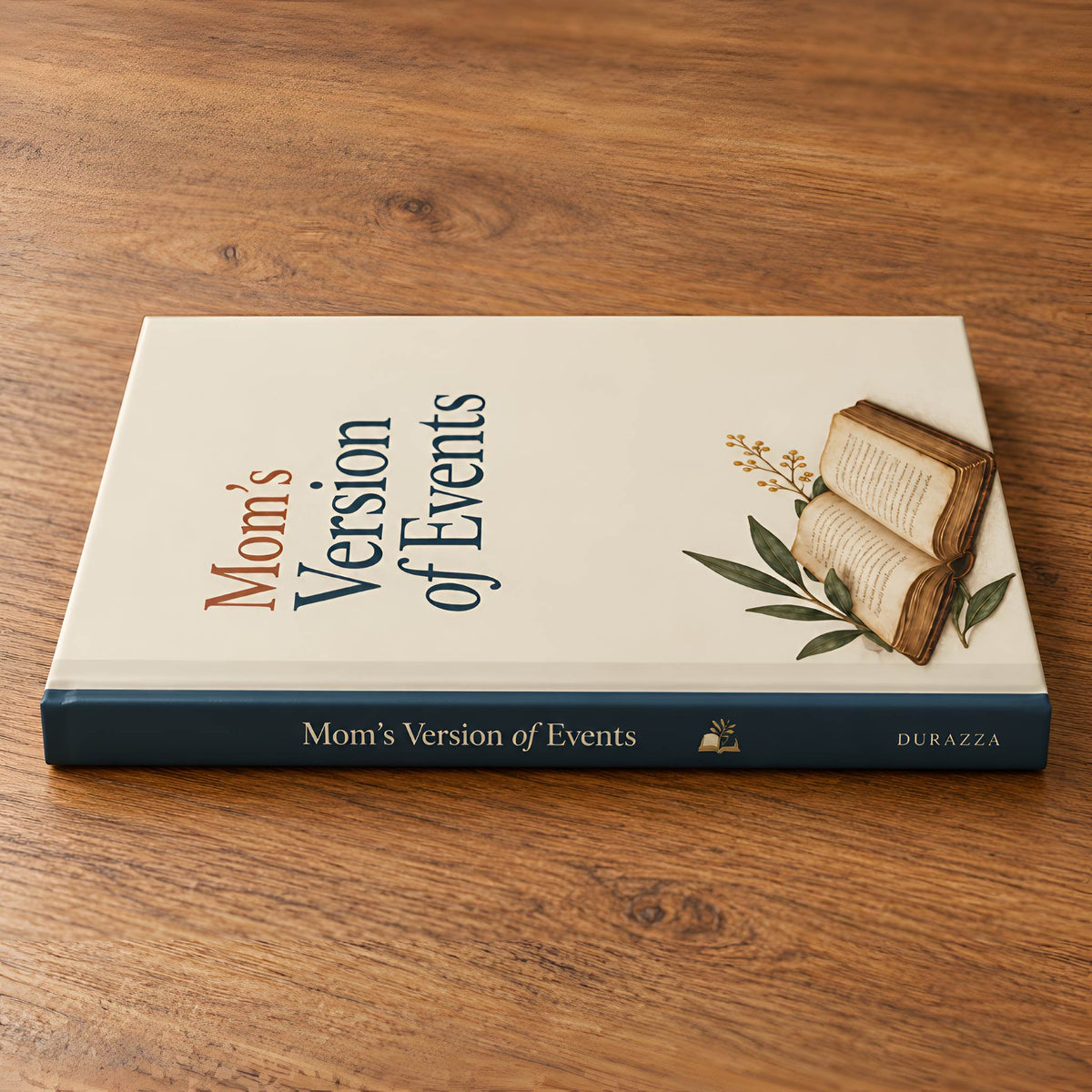 A hardcover journal titled "Mom's Version of Events" resting on a wooden tabletop. The cover is cream with a navy blue spine and a small illustration of an open book with leaves.
