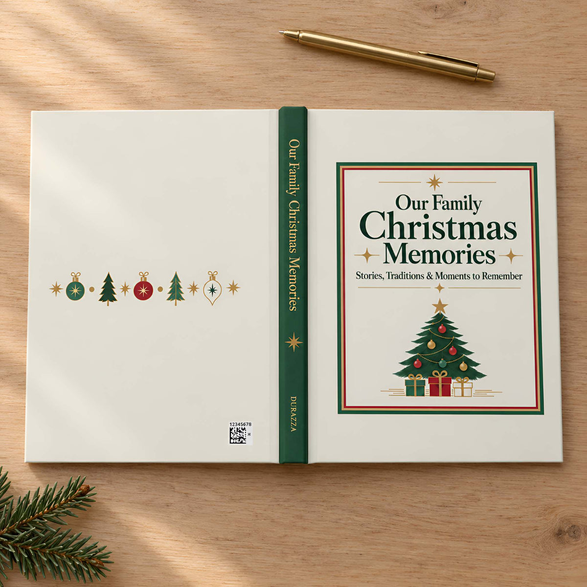 An open hardcover book titled "Our Family Christmas Memories" lies on a light wood tabletop, with a gold pen above and pine branches in the lower left corner. The cover is off-white with a green spine and a festive Christmas tree illustration on the right page.