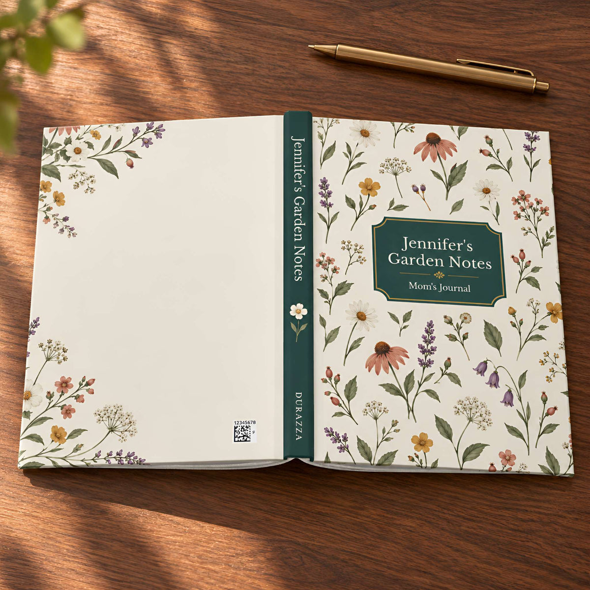 An open floral garden journal titled 'Jennifer's Garden Notes' lies on a wooden tabletop with a gold pen nearby. The notebook cover and inner pages feature a delicate multicolor wildflower pattern on an off-white background, with a dark green spine and title panel.