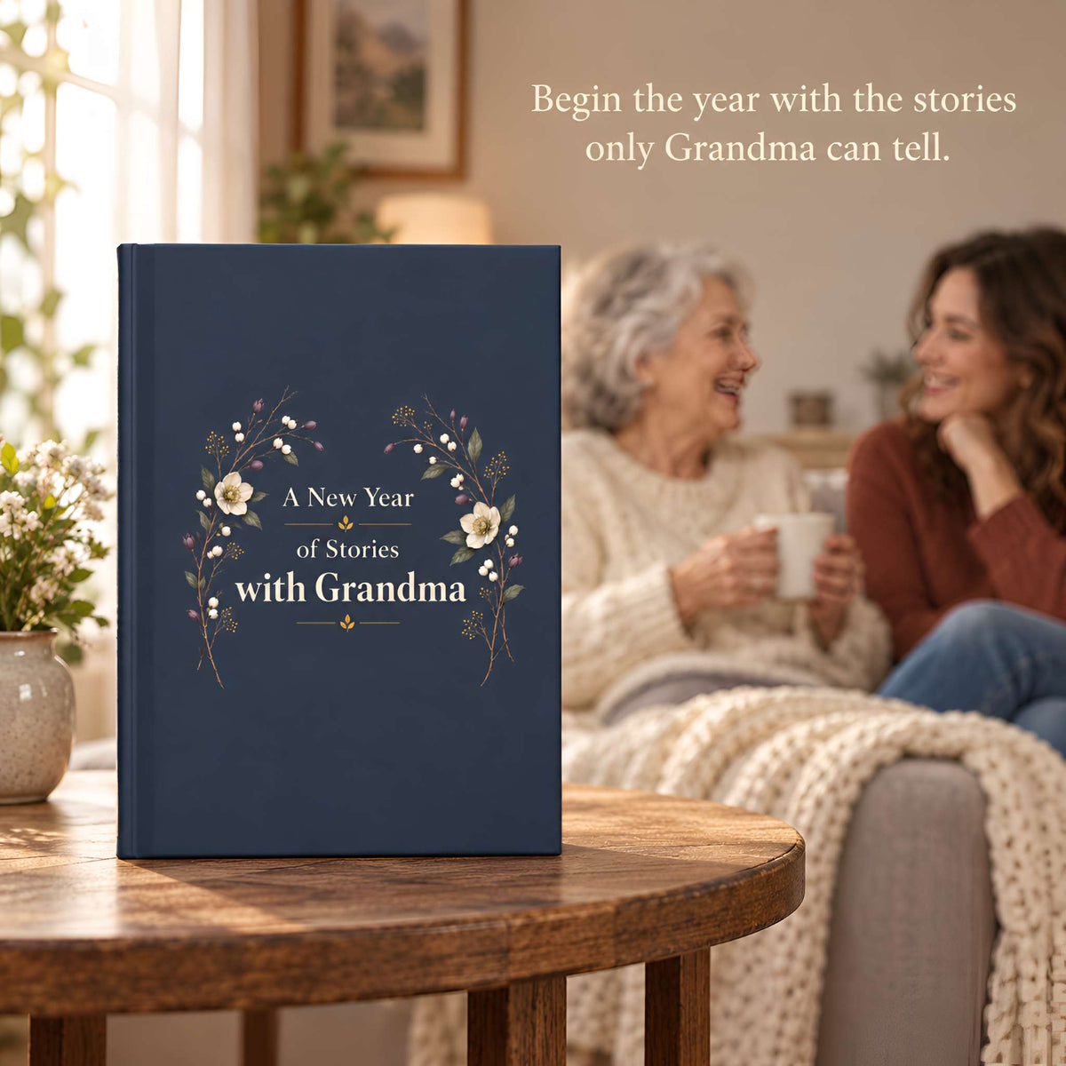 A navy blue hardcover journal standing on a wooden table in a cozy living room, with an elderly woman and a younger woman sitting in the background holding mugs.