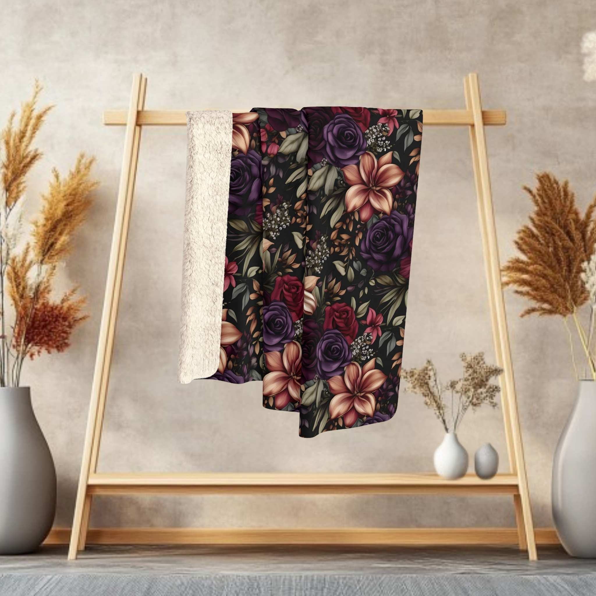 Floral-patterned blanket on a wooden rack with decorative vases and plants against a neutral wall.