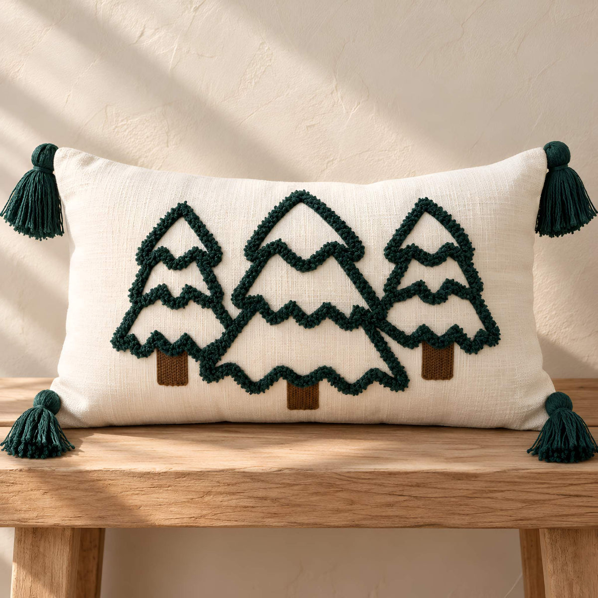 Ivory embroidered tree lumbar pillow cover with dark green corner tassels displayed on a wooden bench.