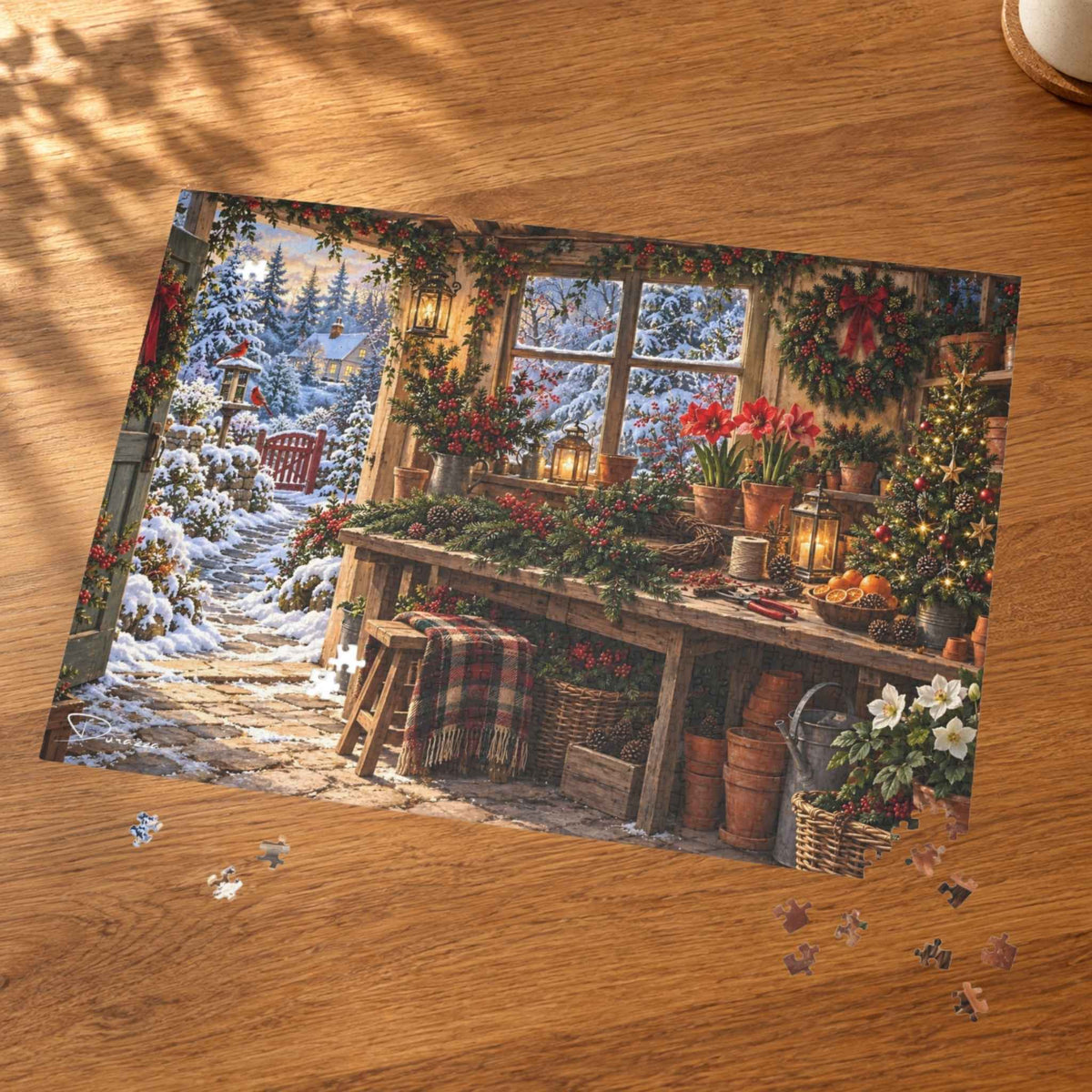 A completed jigsaw puzzle showing a cozy Christmas garden cabin scene with snow outside and holiday decorations inside, placed on a wooden tabletop with a few loose puzzle pieces nearby.