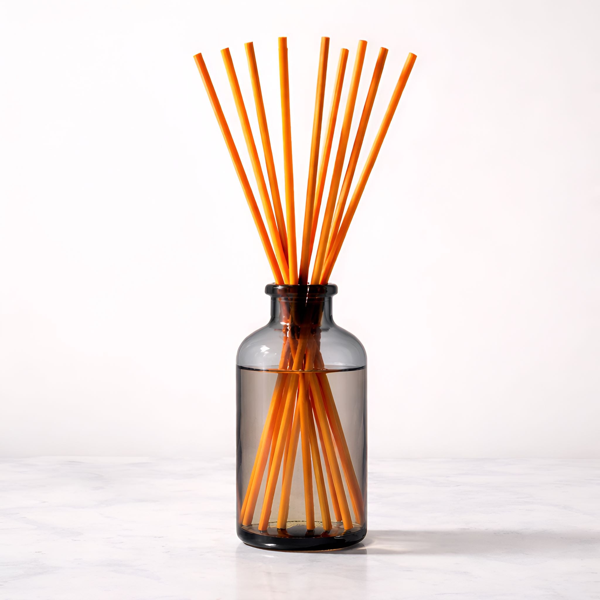 Glass diffuser bottle with orange reeds on a white background