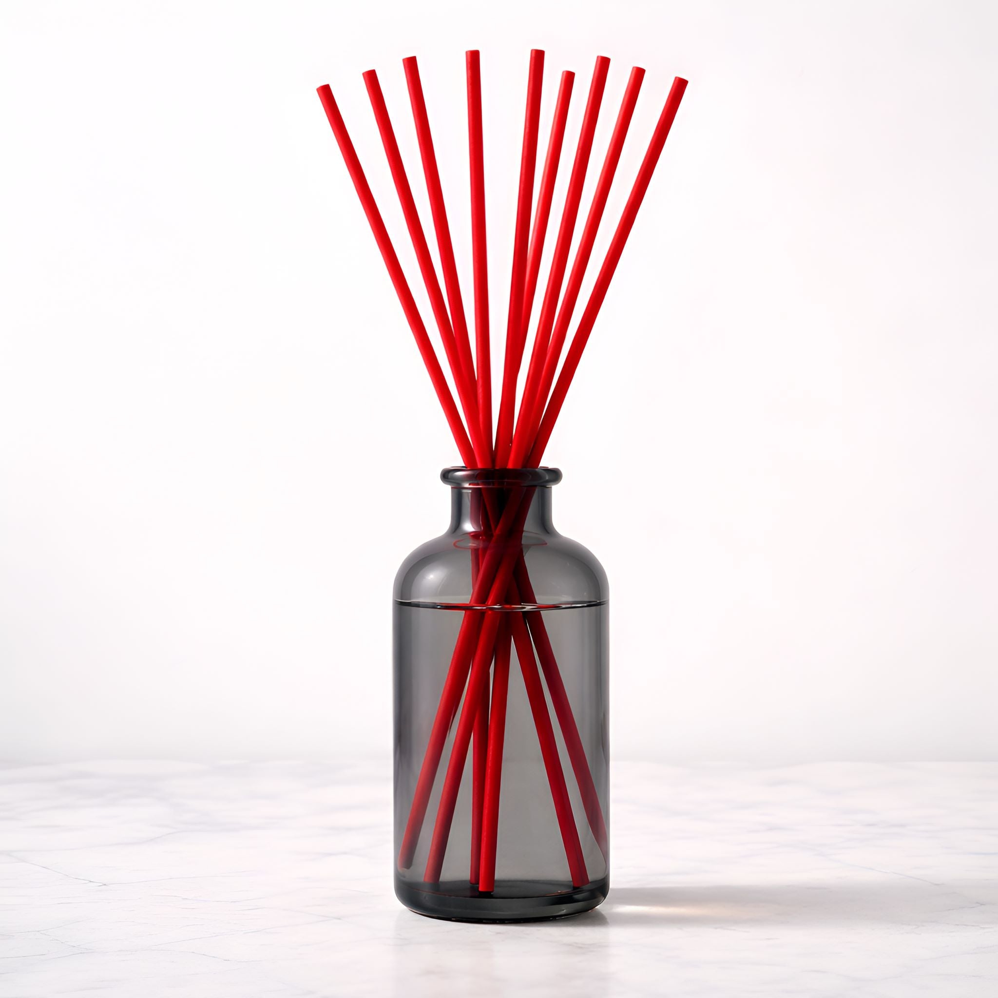 Black glass diffuser bottle with red diffuser sticks on a white background