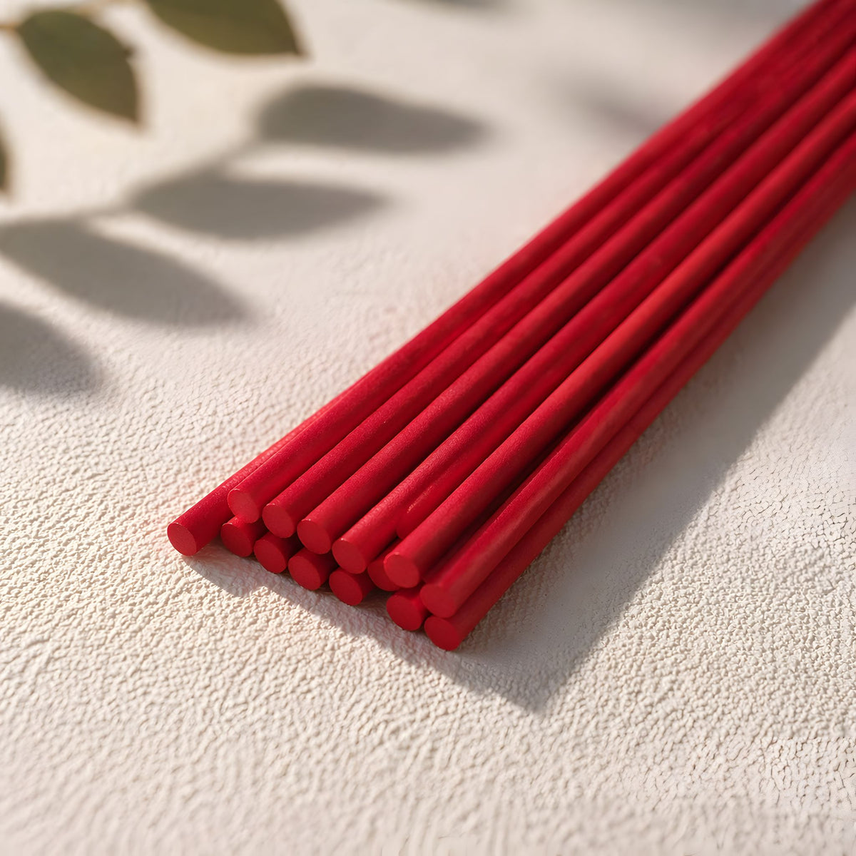 12 inch red diffuser reeds on a textured white surface with a natural light background