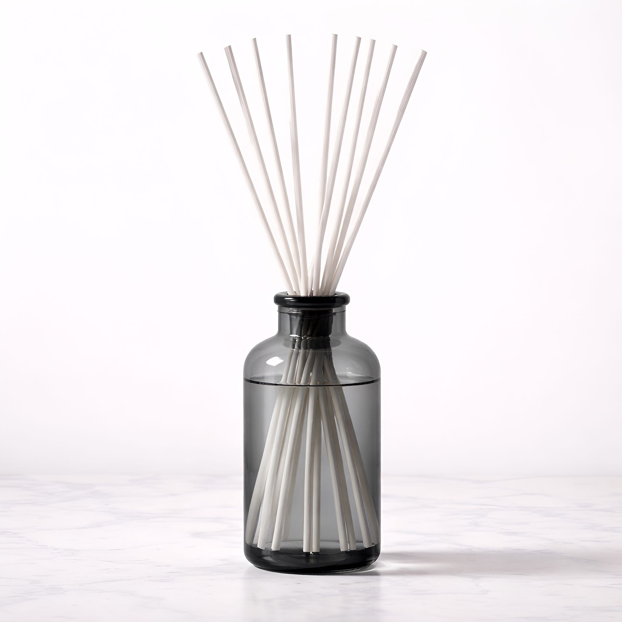 Diffuser with white reed sticks in a dark glass bottle on a white background