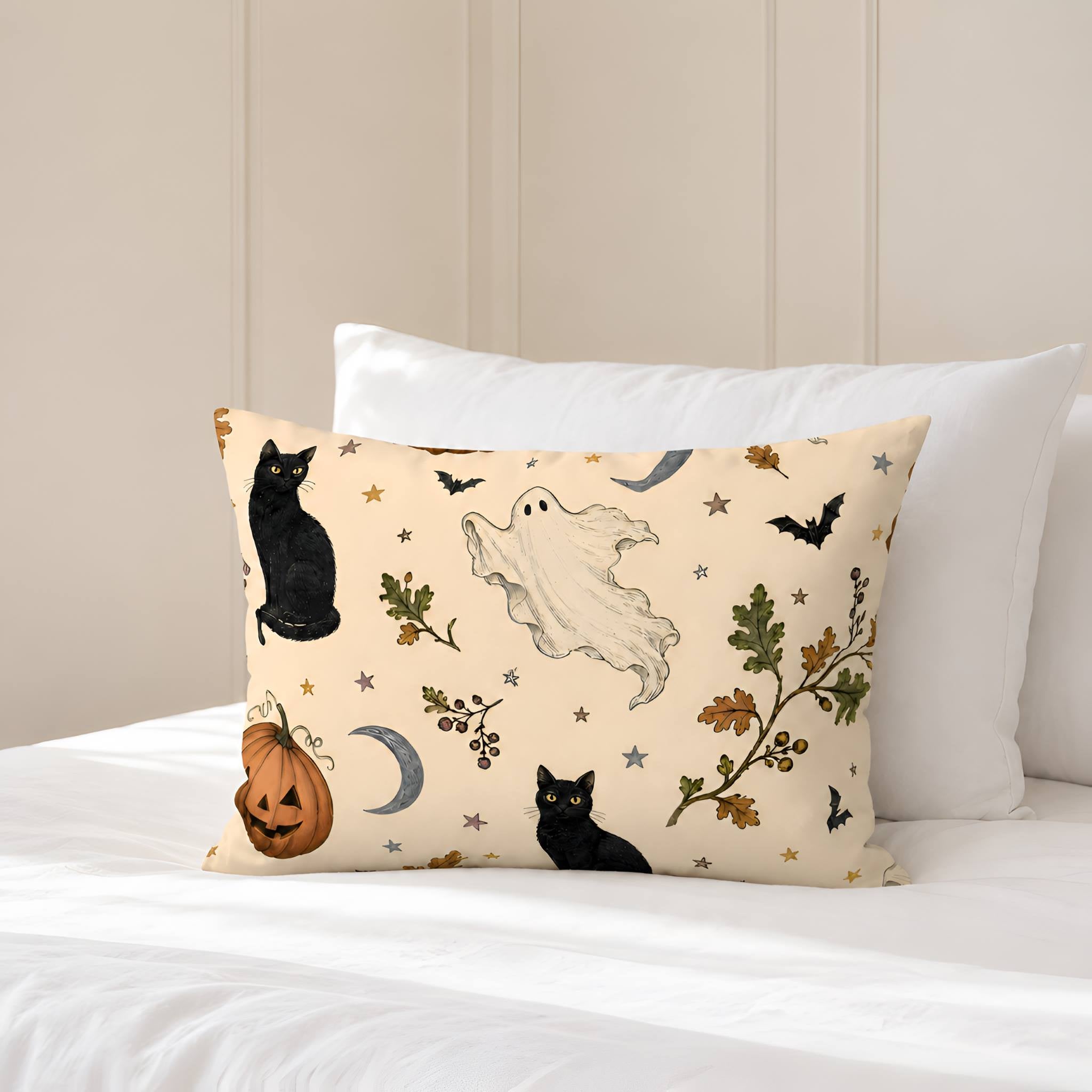 A pillow sham with a Halloween cream print featuring black cats, a white ghost, a pumpkin, bats, and leaves, styled on a bed with white bedding and a neutral paneled wall background.