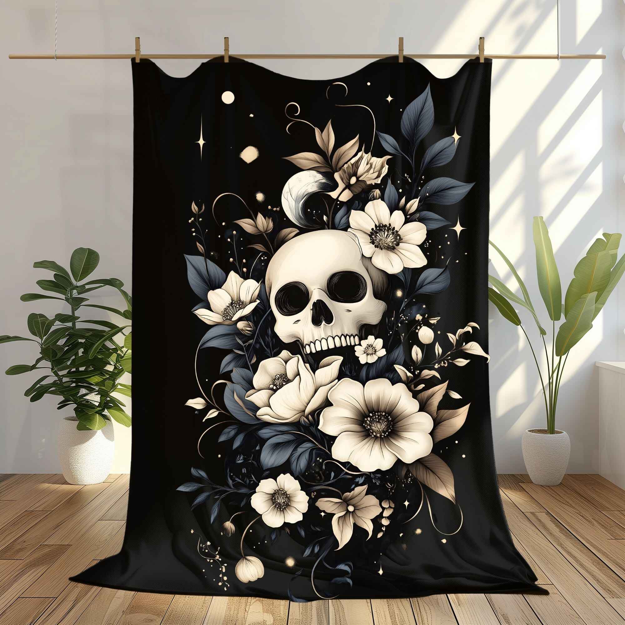 A throw blanket featuring a skull surrounded by intricate flowers and celestial elements, displayed on a wooden floor with a plant in the background.