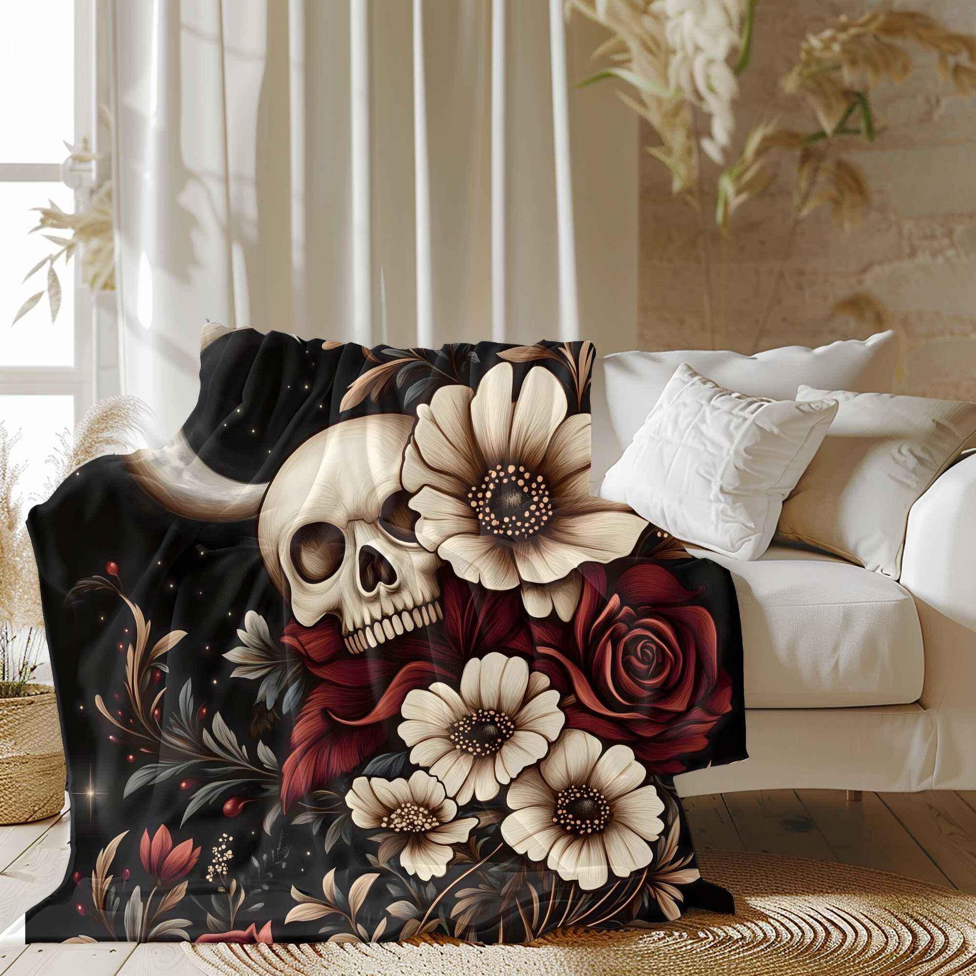 A cozy throw blanket with a gothic boho design, featuring a floral skull with daisies and roses on a crescent moon background, draped over a sofa in a room with parlor plants and a white wall.