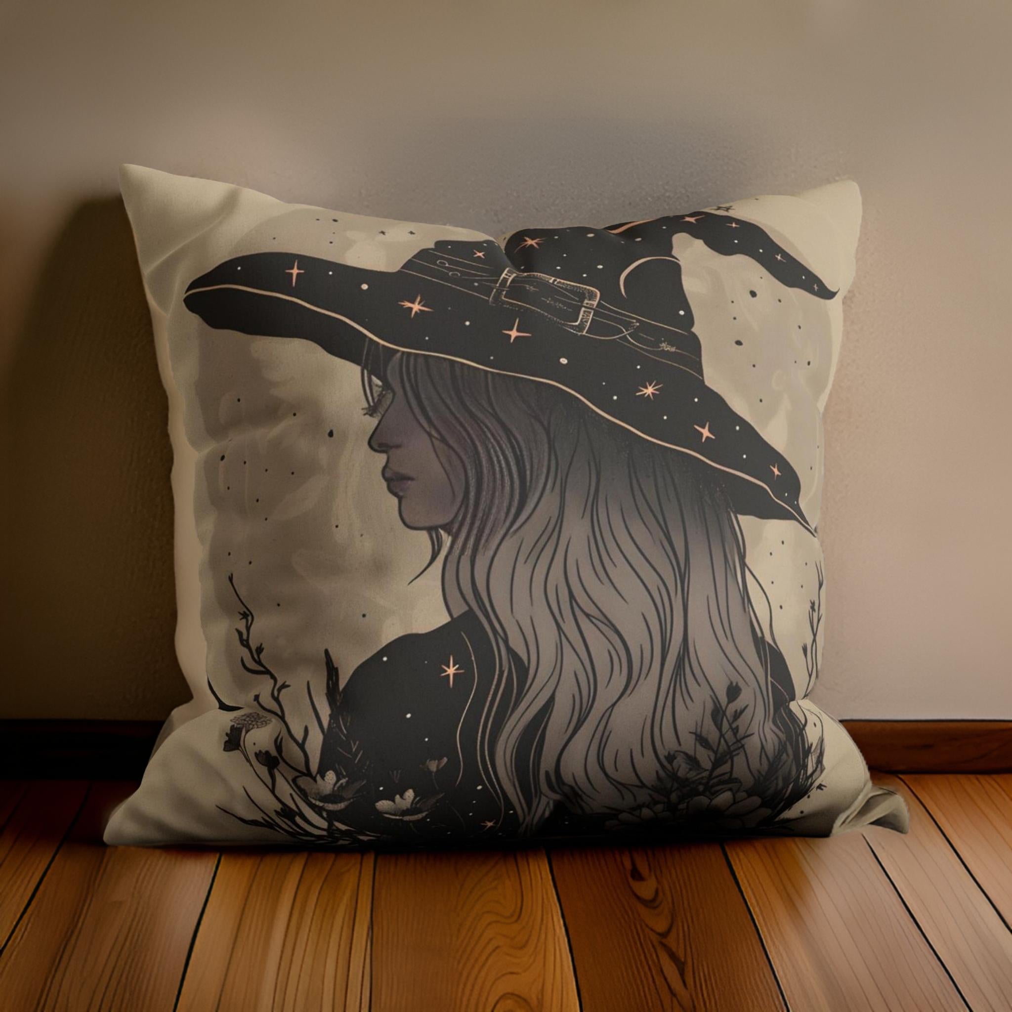 A throw pillow with a whimsical illustration of a witch's face and a hat with stars and moons on a dark beige background, placed on a wooden floor.