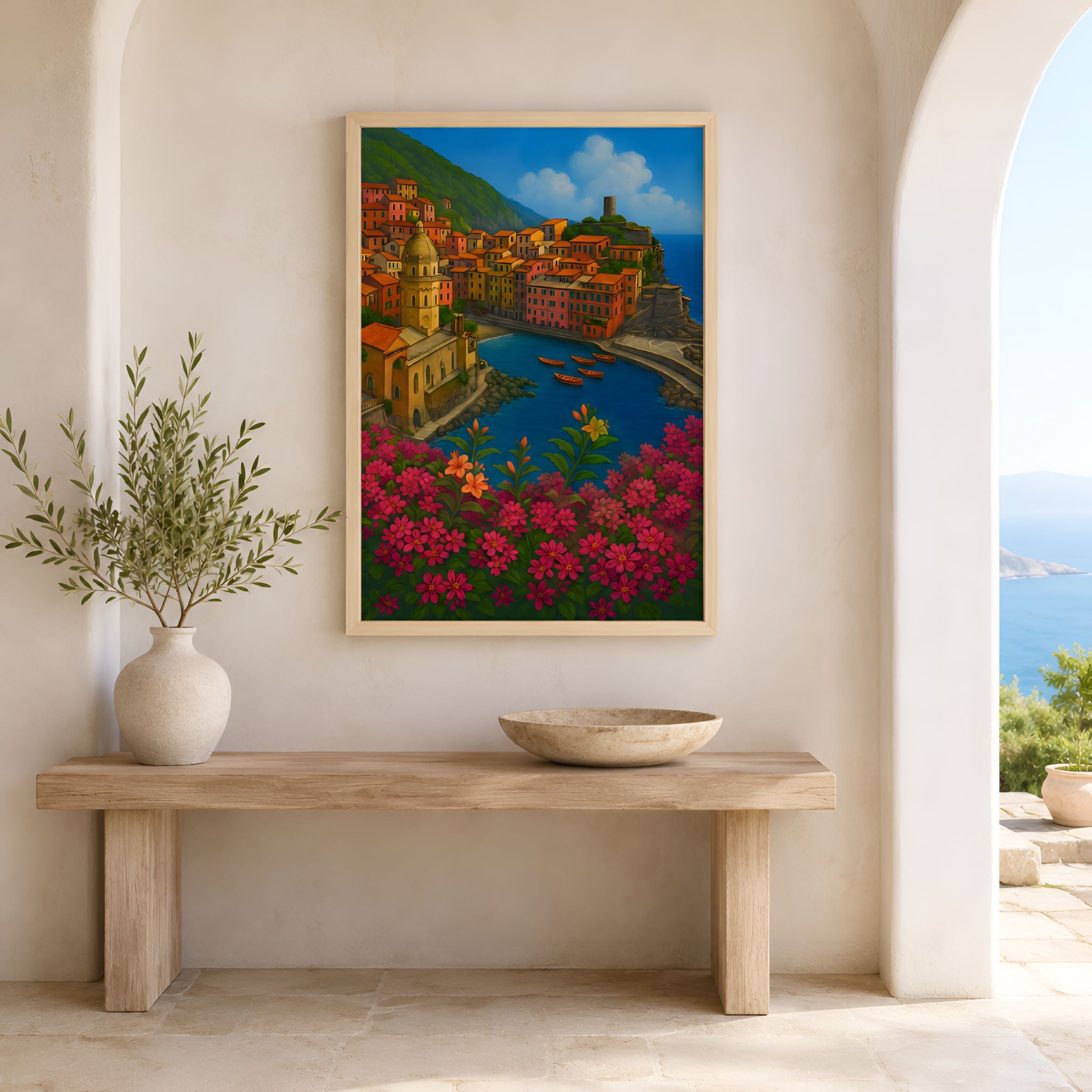 Framed wall artwork of an Italian coastal village on the Mediterranean with flowers on a wall above a wooden bench.