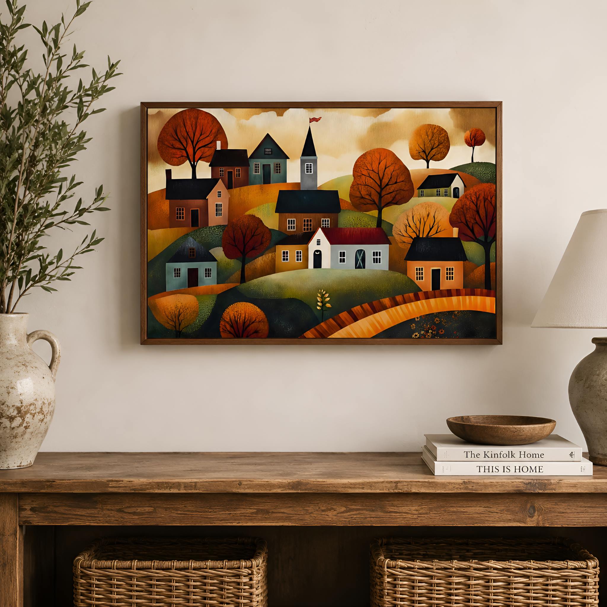 Walnut framed wall art of a folk art village scene on a wall above a wooden console table.