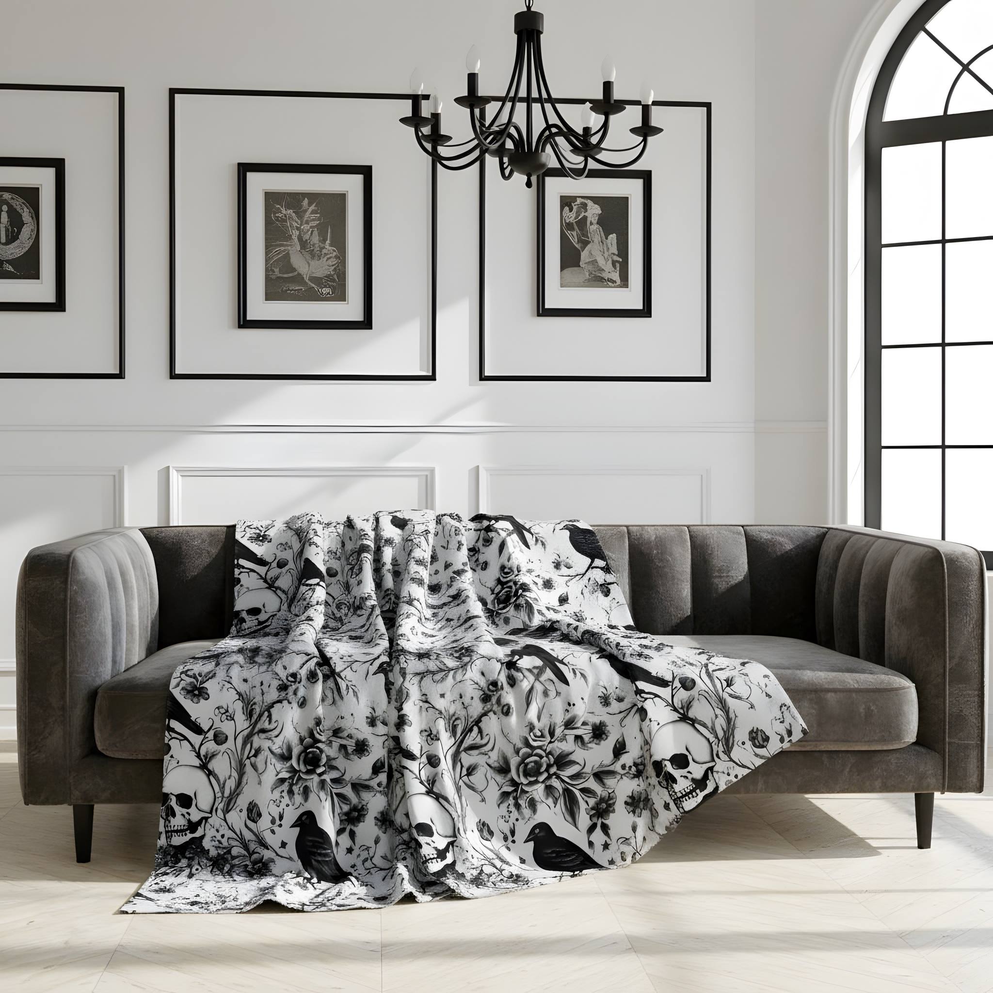 Black and white gothic velveteen throw blanket with skull, raven, and floral print draped on sofa.