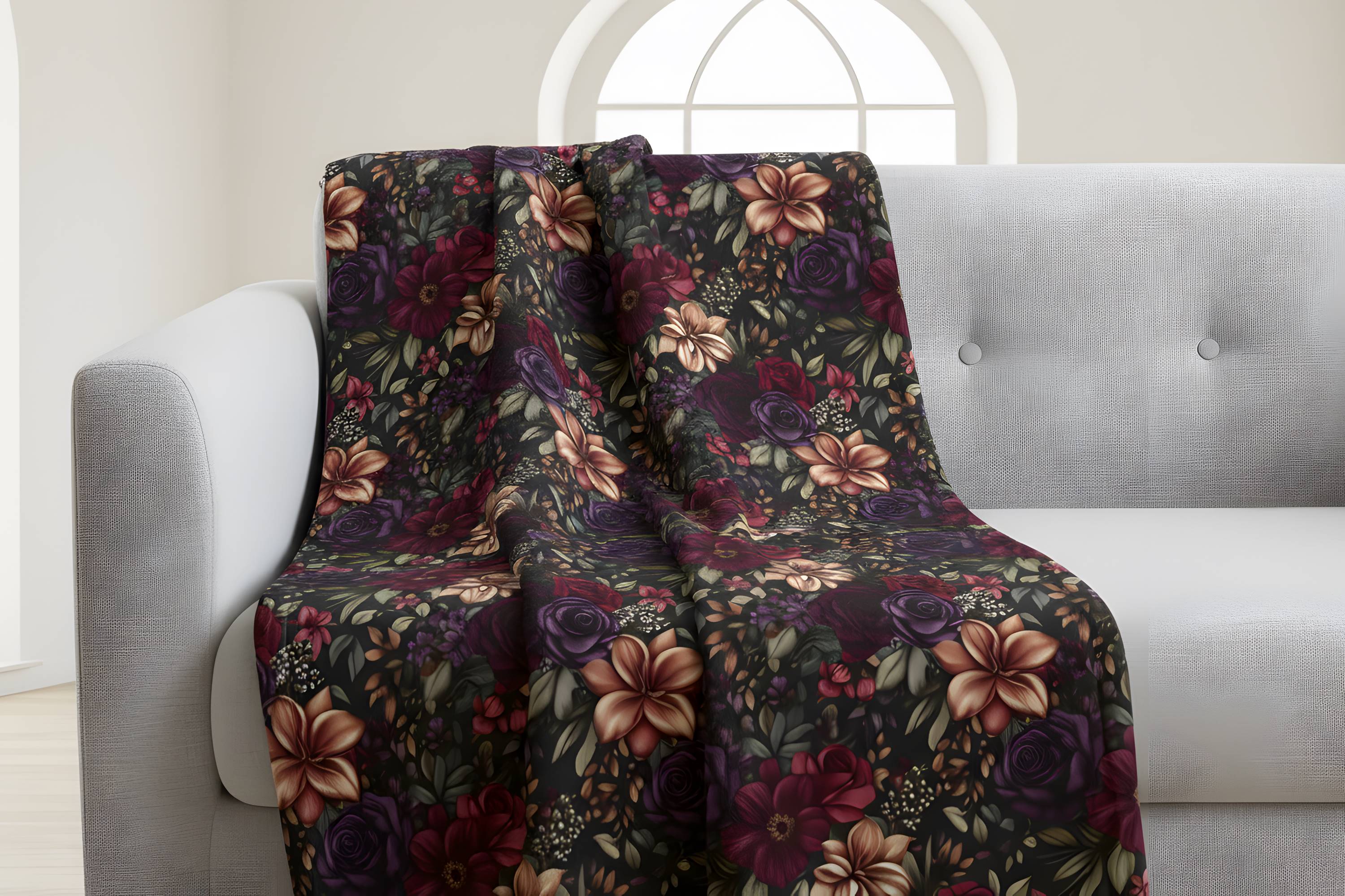 Moody flower throw blanket draped over a light sofa with rich floral print on black.