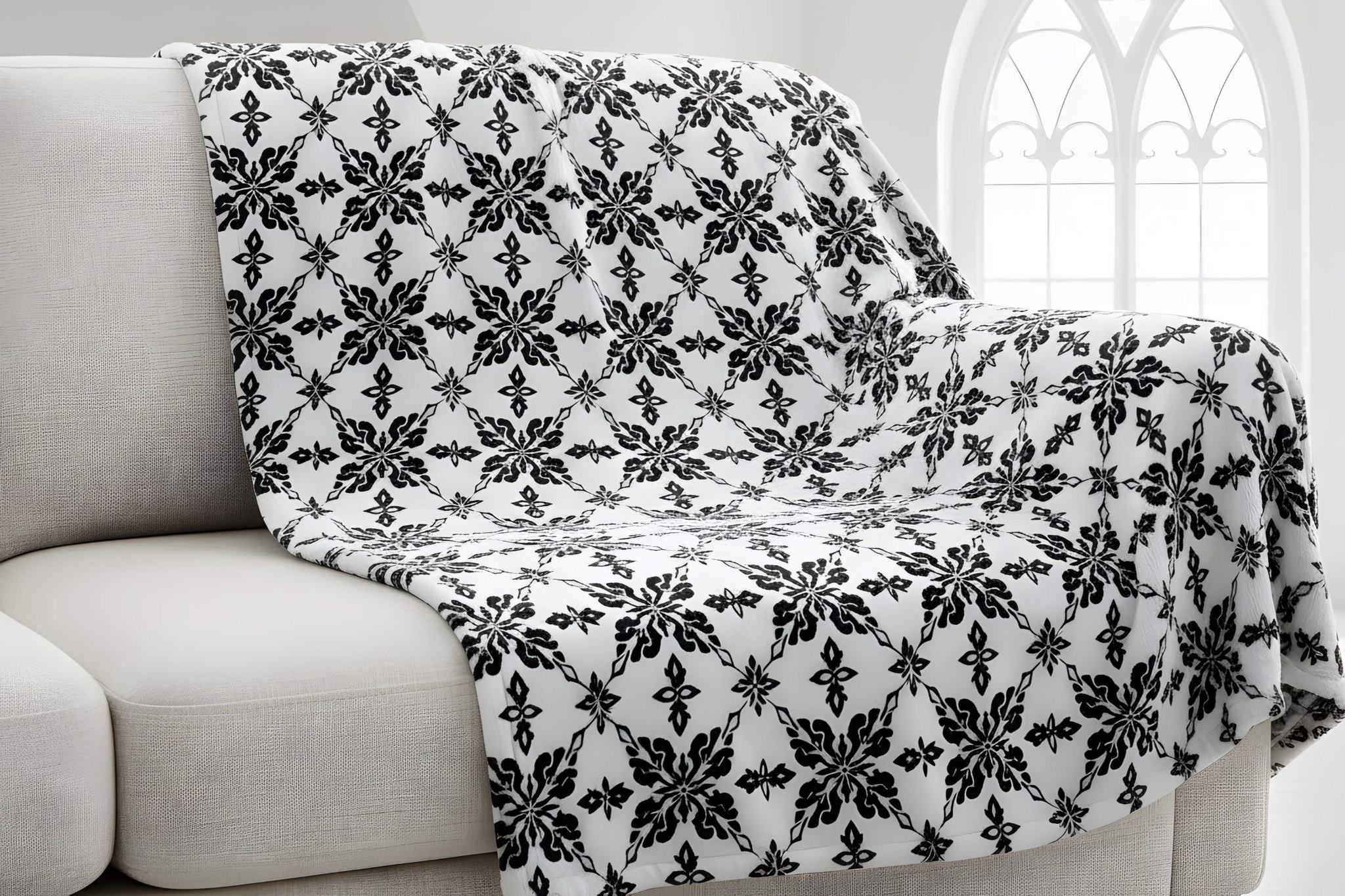 Black and white damask throw blanket is draped over a light-colored sofa.