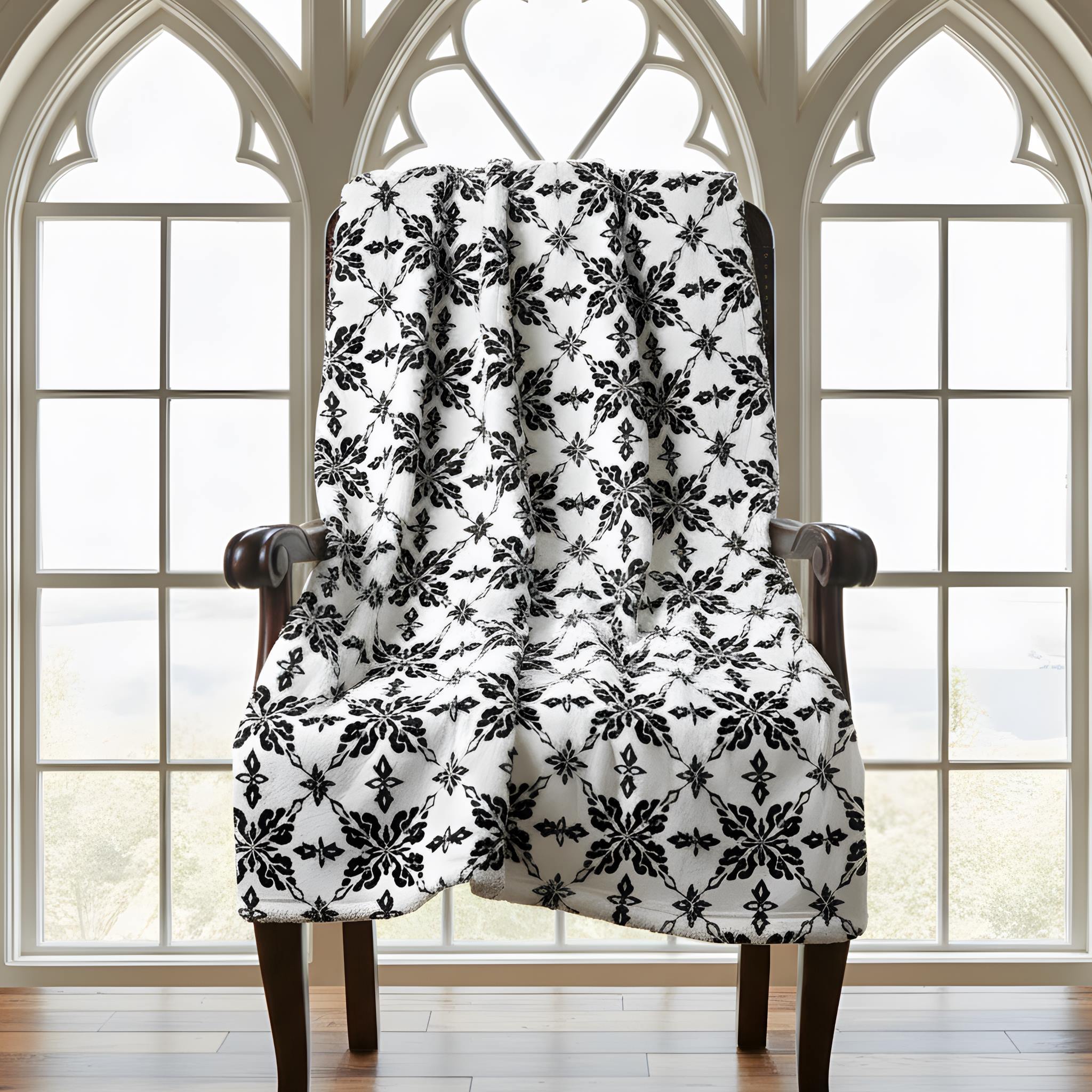 Black-and-white damask throw blanket draped over a chair in front of large gothic windows.