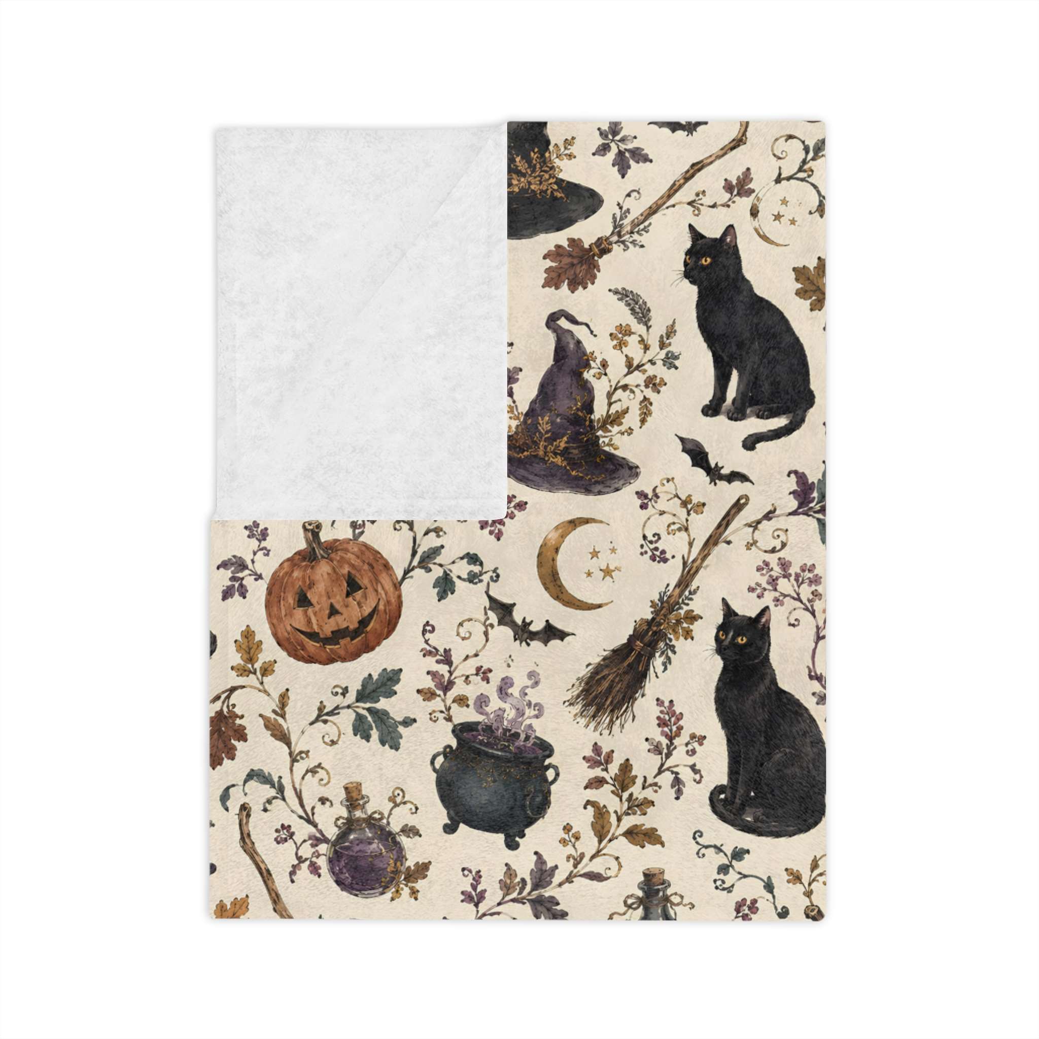 A folded Halloween blanket on an ivory background with black cats, a witch hat, broom, cauldron, bats, moon, pumpkins, and autumn leaves. One corner is turned to reveal a solid off-white textured reverse side.
