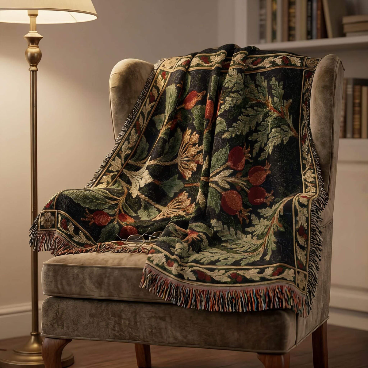 A woven throw blanket with a botanical tapestry pattern draped over a gray velvet armchair in a cozy room setting next to a floor lamp.