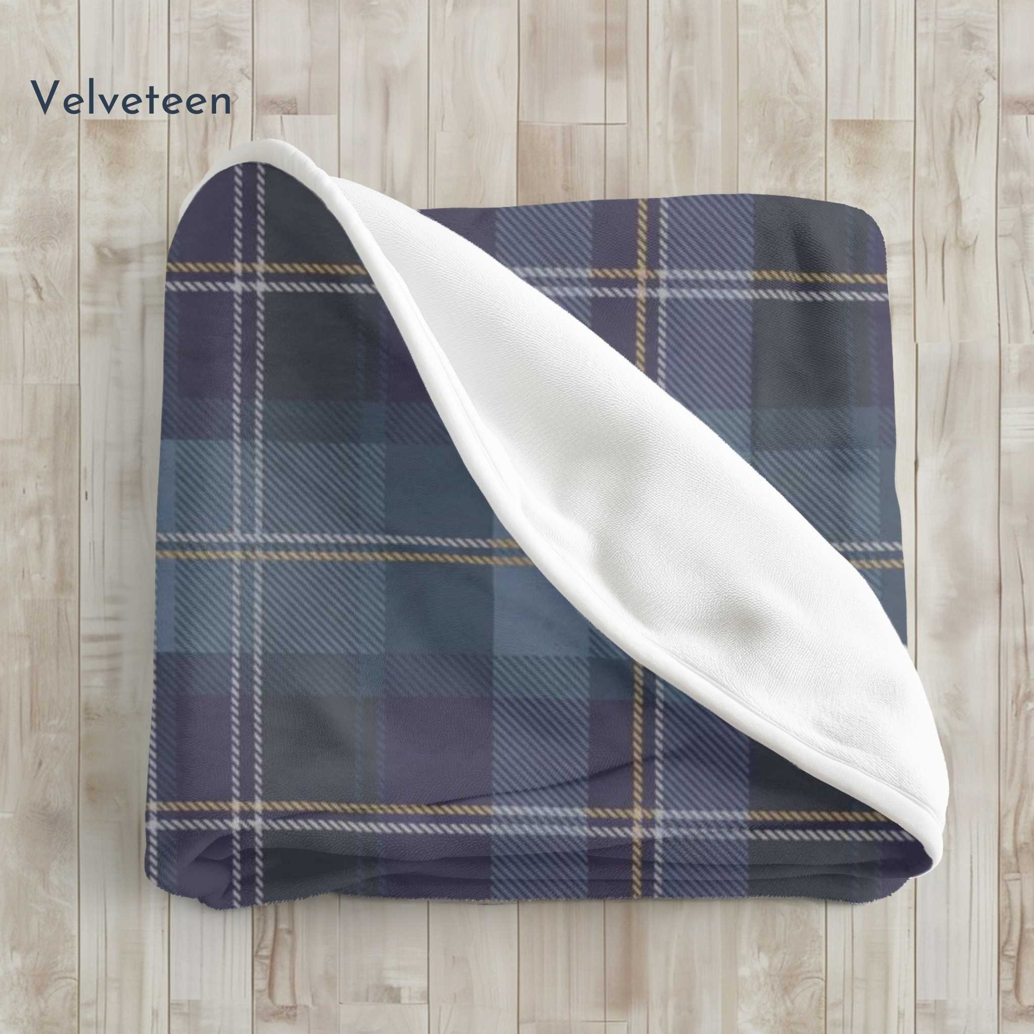 Blue plaid blanket with white reverse side on a wooden surface, branded 'Velveteen'.