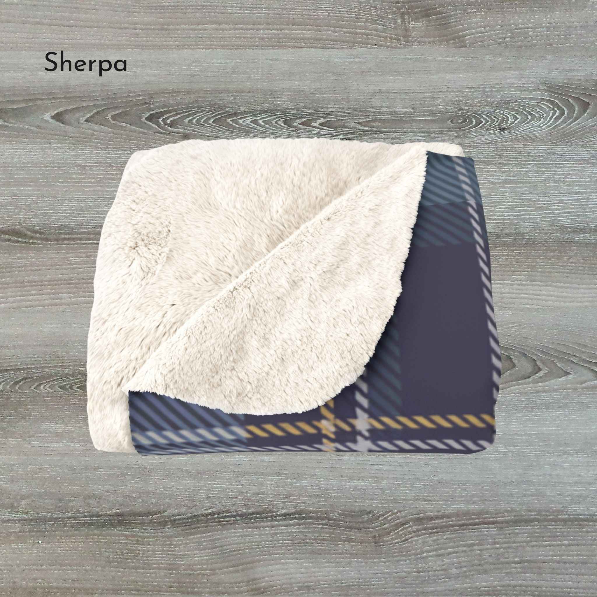 Folded Sherpa blanket with plaid pattern on a wooden surface