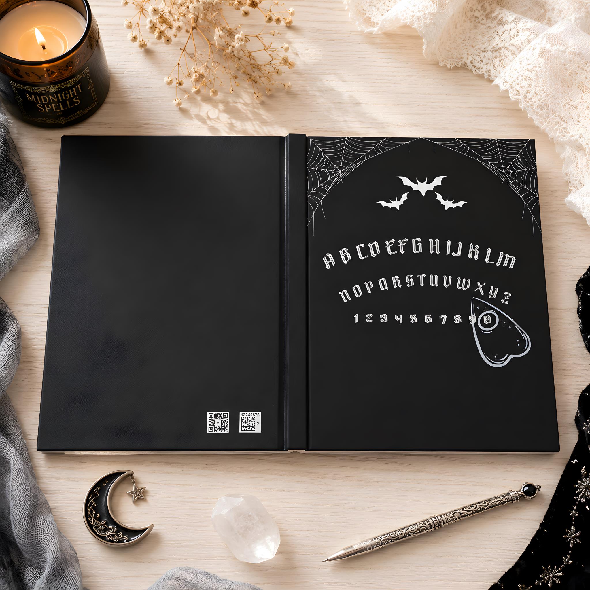 Black notebook with Ouija board design on a wooden surface with decorative items.