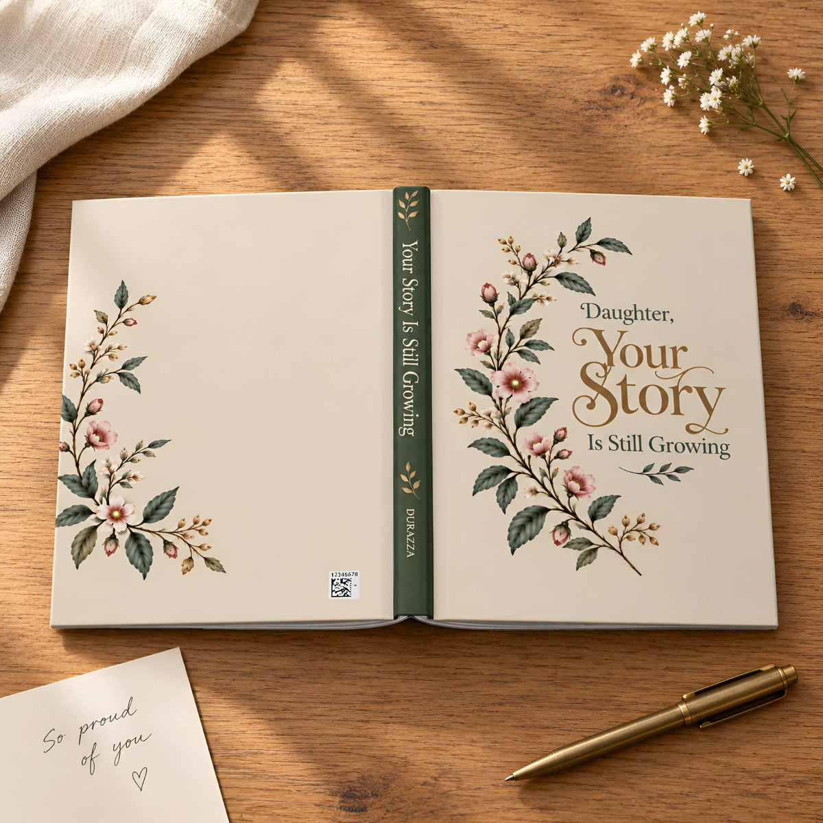 An opened journal a gift to your daughter with floral illustrations and the text 'Daughter, Your Story Is Still Growing' on the cover, displayed on a wooden tabletop with a pen, fabric, and small flowers around it.