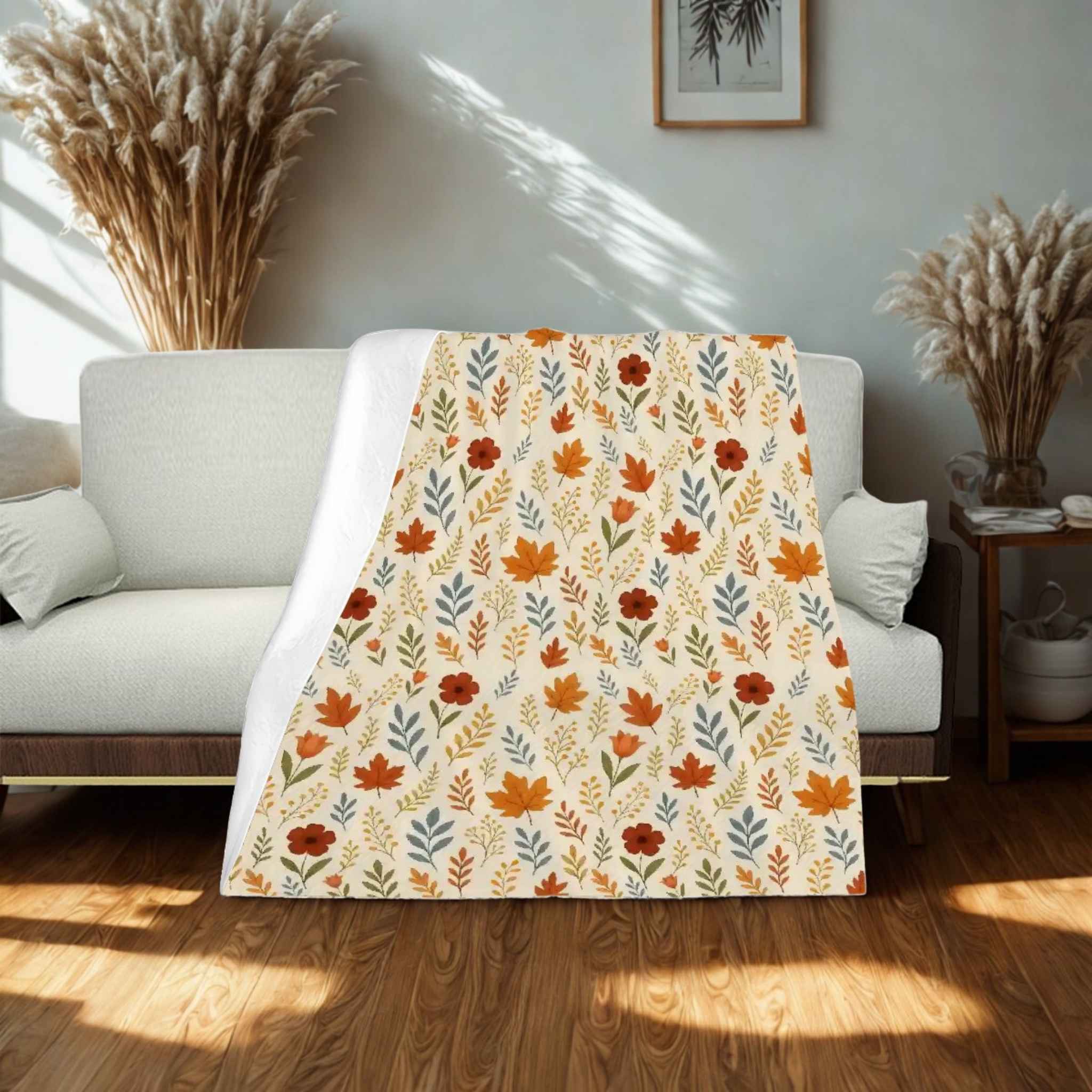 Leaf patterned blanket draped over a white sofa in a room with wooden flooring and decorative elements.