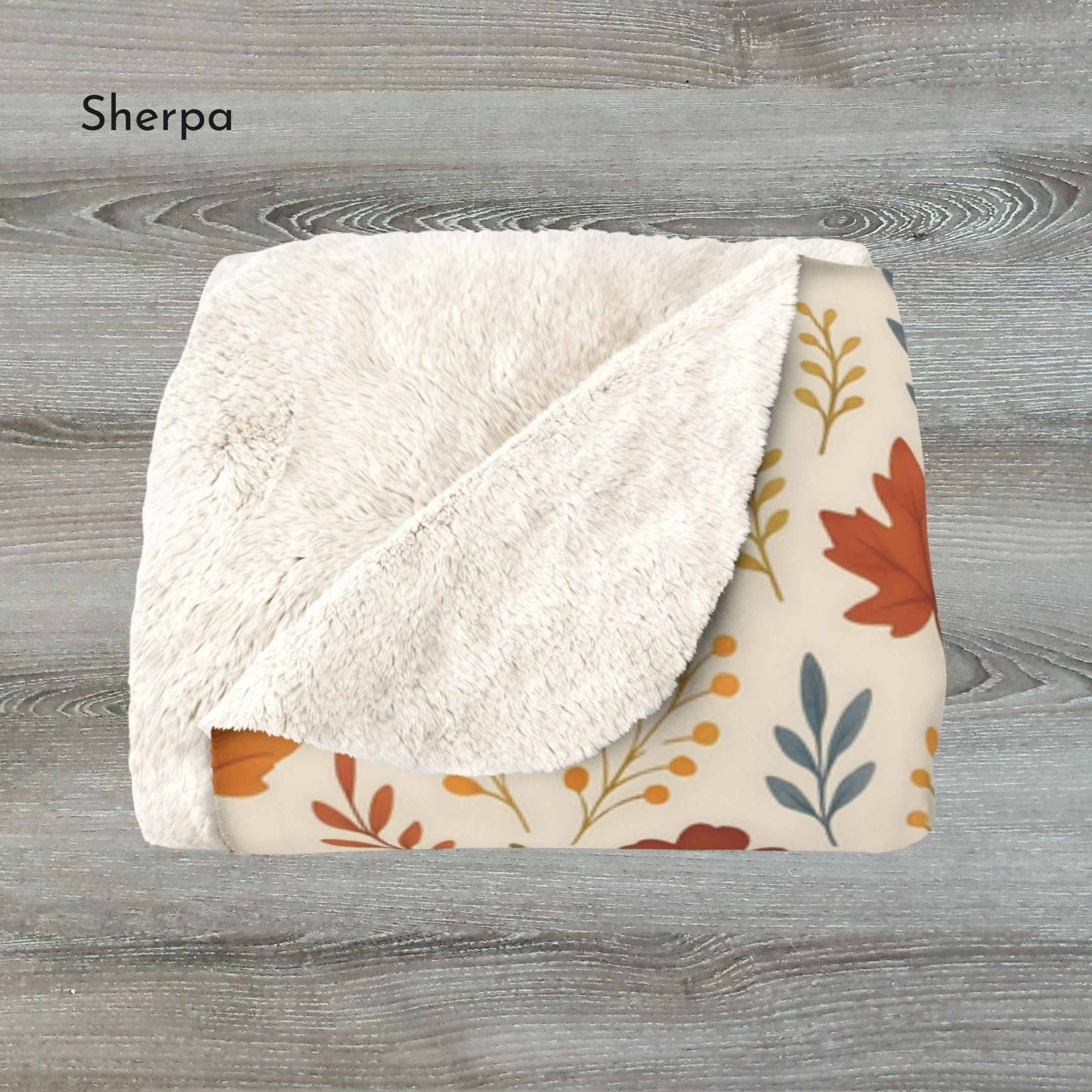 Folded sherpa blanket with floral pattern and leaf pattern on a wooden surface