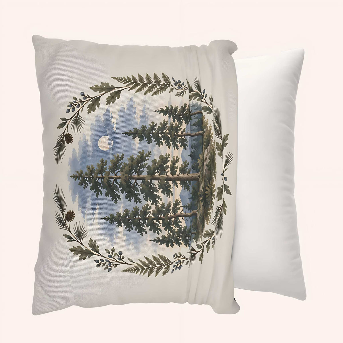 A square decorative pillow cover with a printed forest scene featuring pine trees, a moon, and a leafy wreath border, shown in front of a plain white throw pillow against a light beige background.