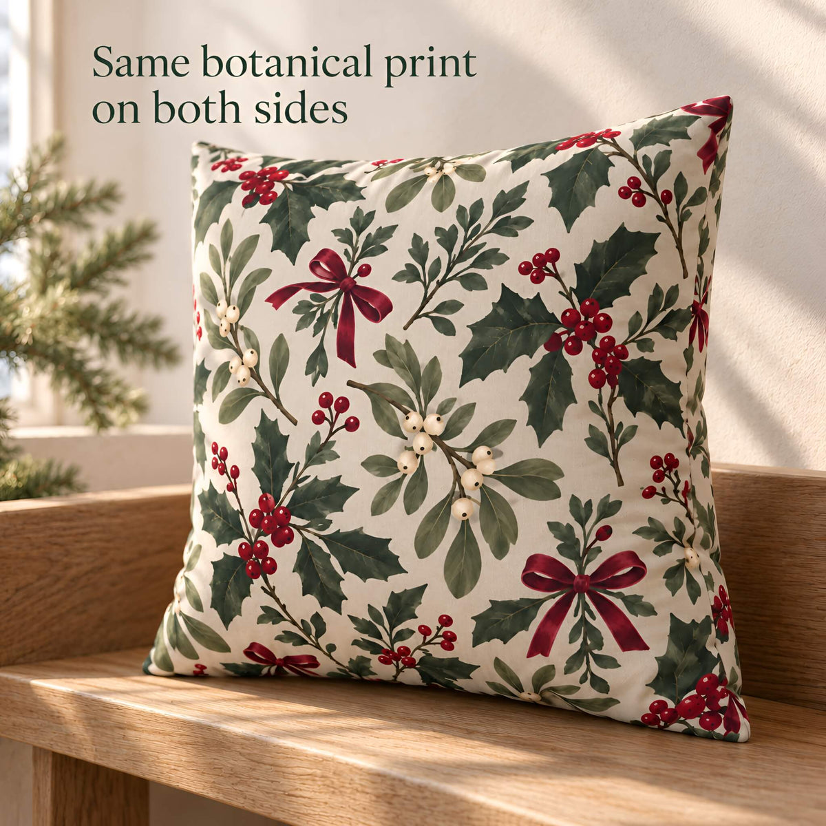 A square decorative pillow cover with a botanical holly print sits on a wooden bench in a sunlit room. The print features green holly leaves, red bows, and red berries on an off-white background.