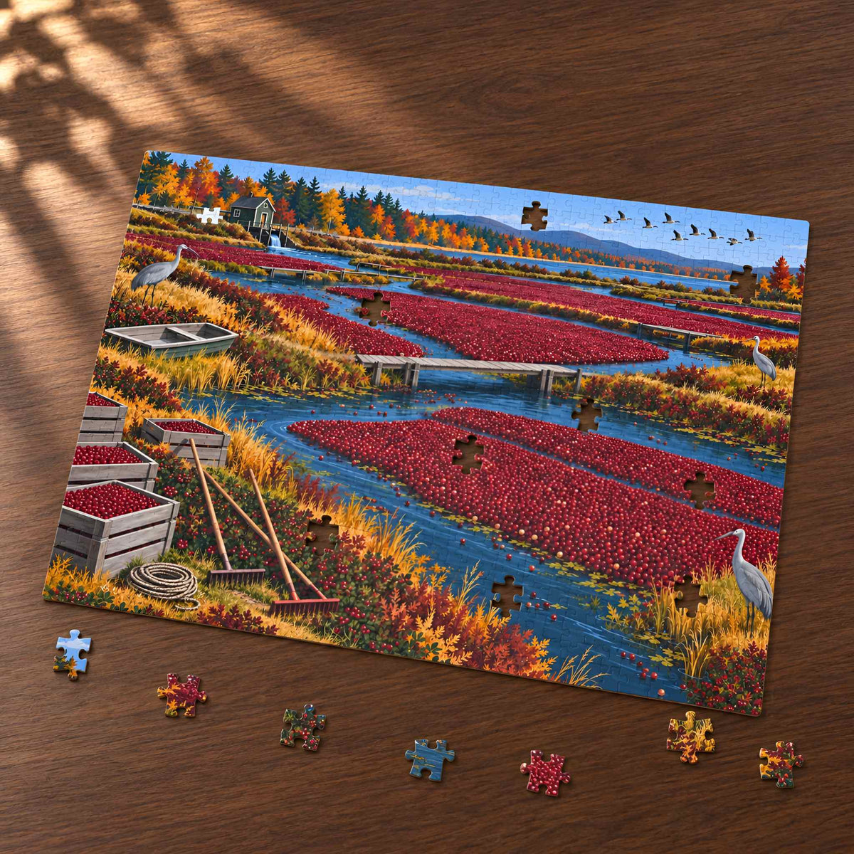 A completed landscape jigsaw puzzle showing a cranberry field with blue waterways, autumn trees, and birds, photographed on a wooden tabletop with a few loose puzzle pieces around it.