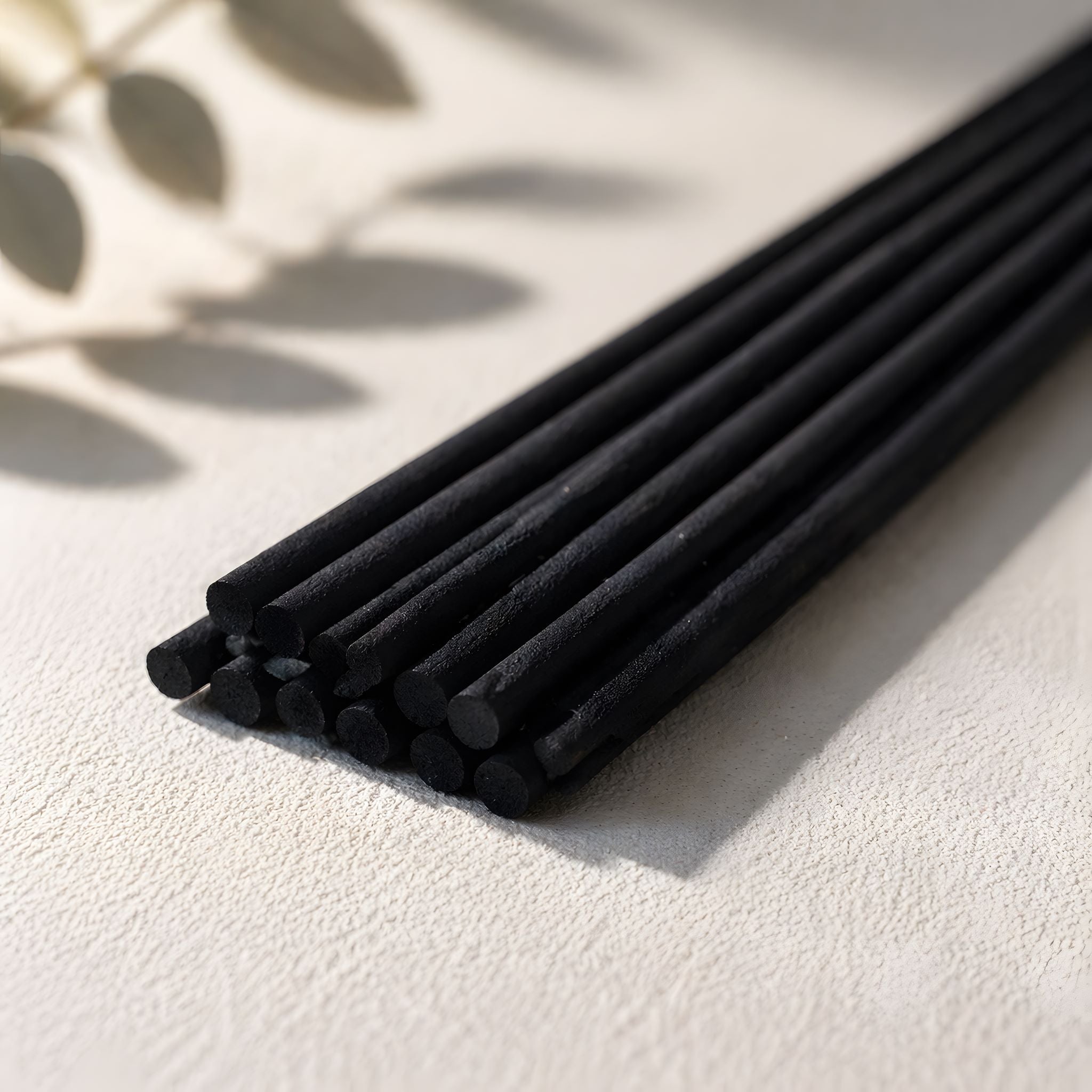 Set of black diffuser sticks on a light surface with a leafy background