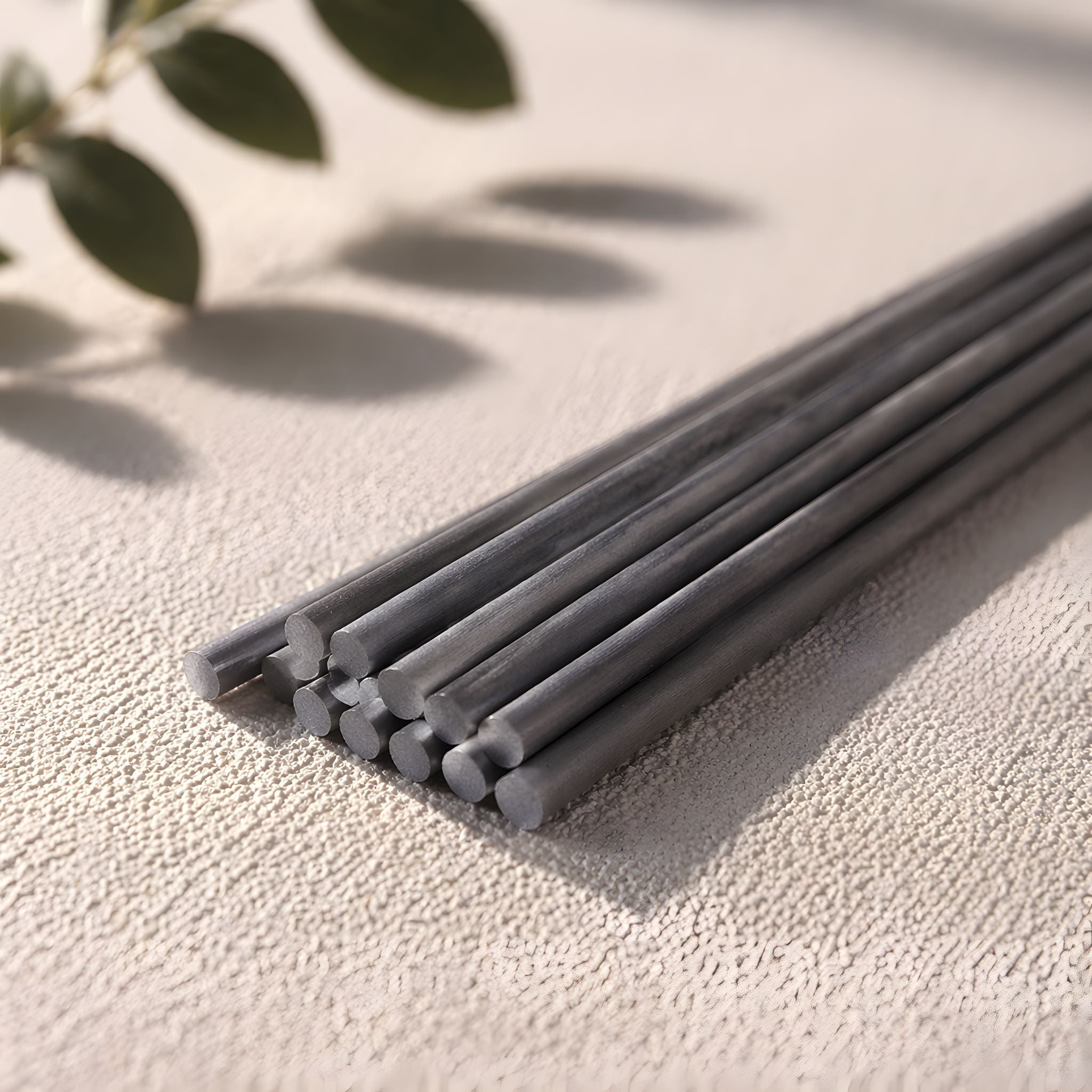 Gray diffuser sticks on a textured surface with green leaves in the background