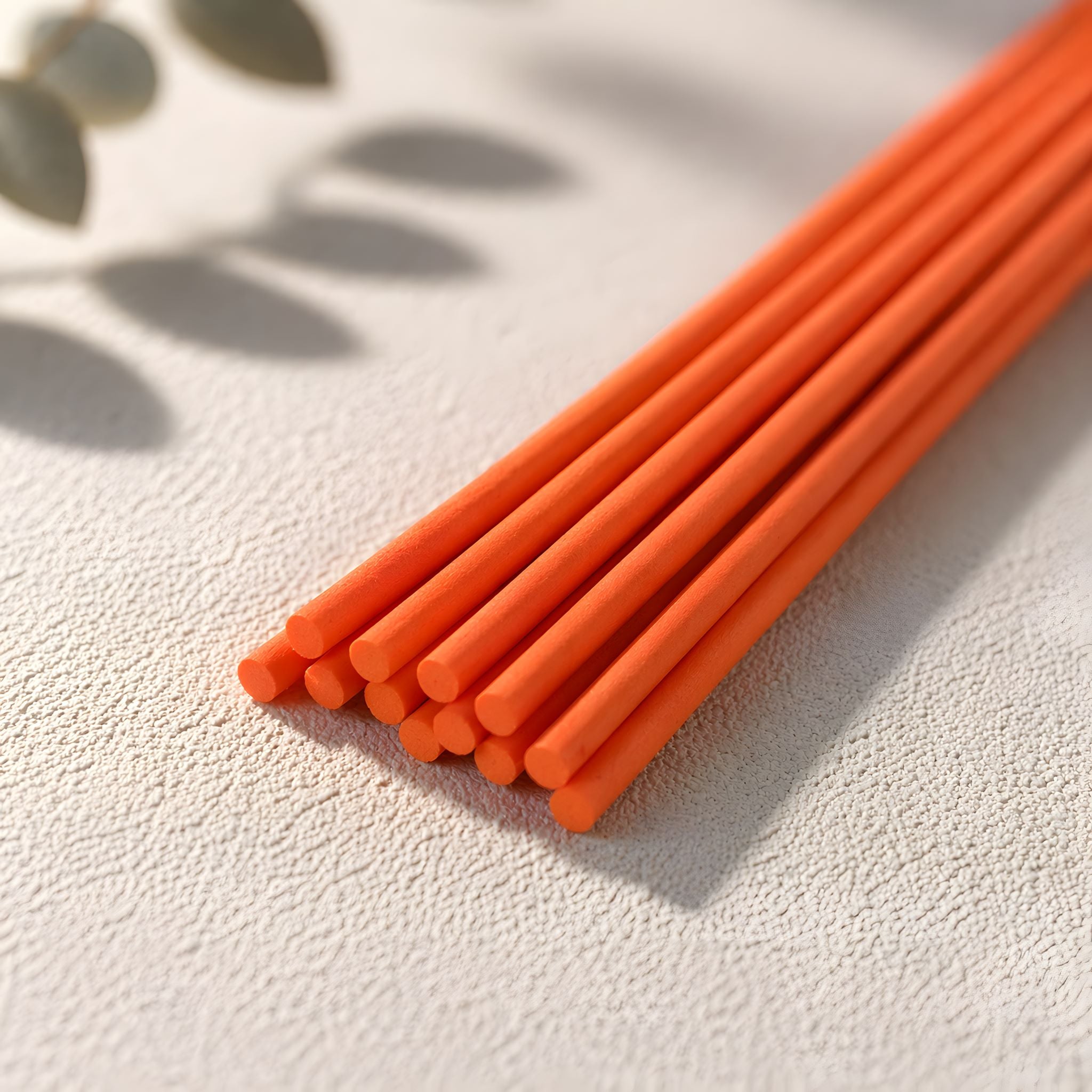 Orange diffuser reeds on a textured surface with leaves in the background