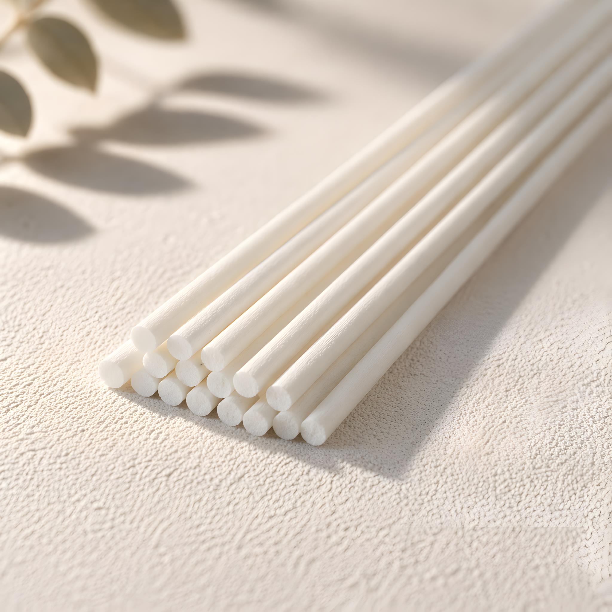 White diffuser sticks on a light beige surface with a natural leaf background