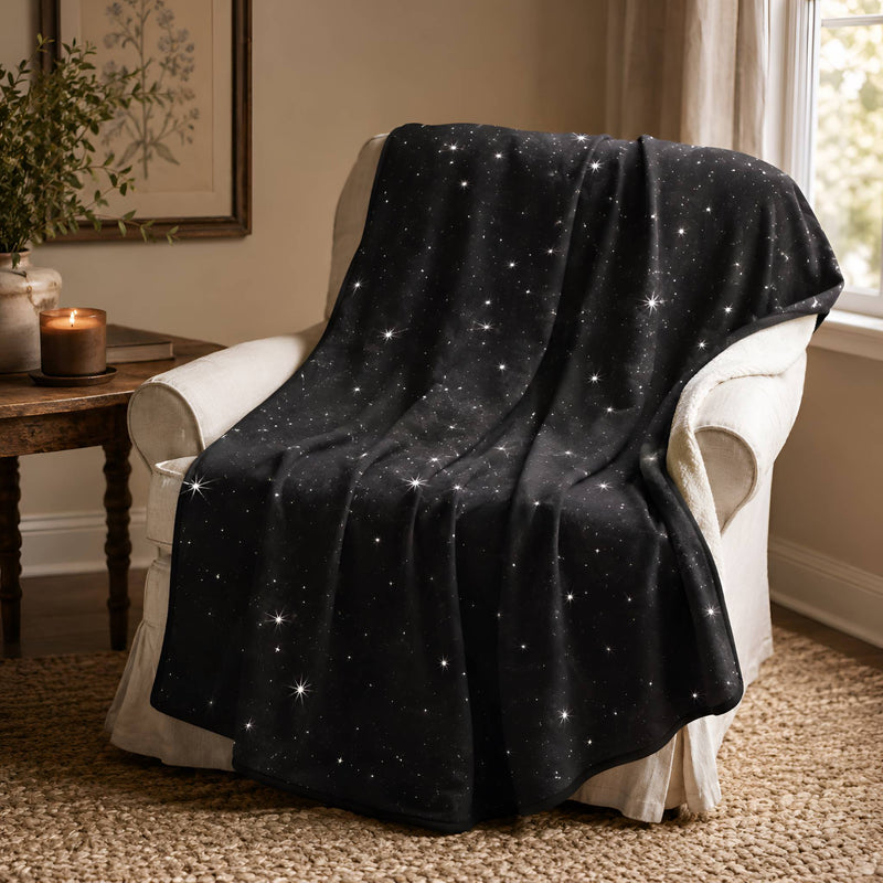 Throw blanket collection with a black celestial blanket draped over a cream chair in a warm cozy home setting.