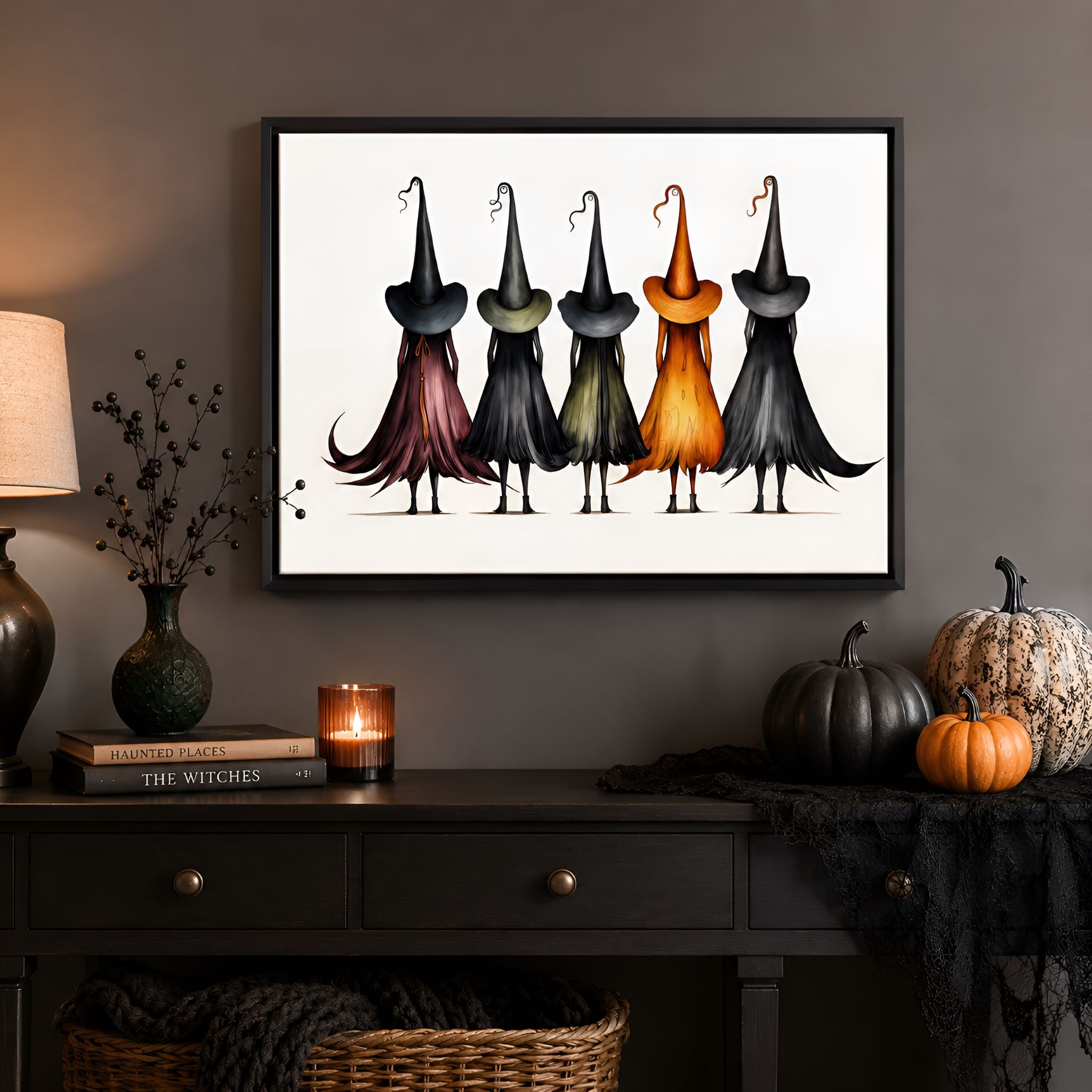 Black framed artwork of witches with colorful hats on a wall above a dark wooden console table.