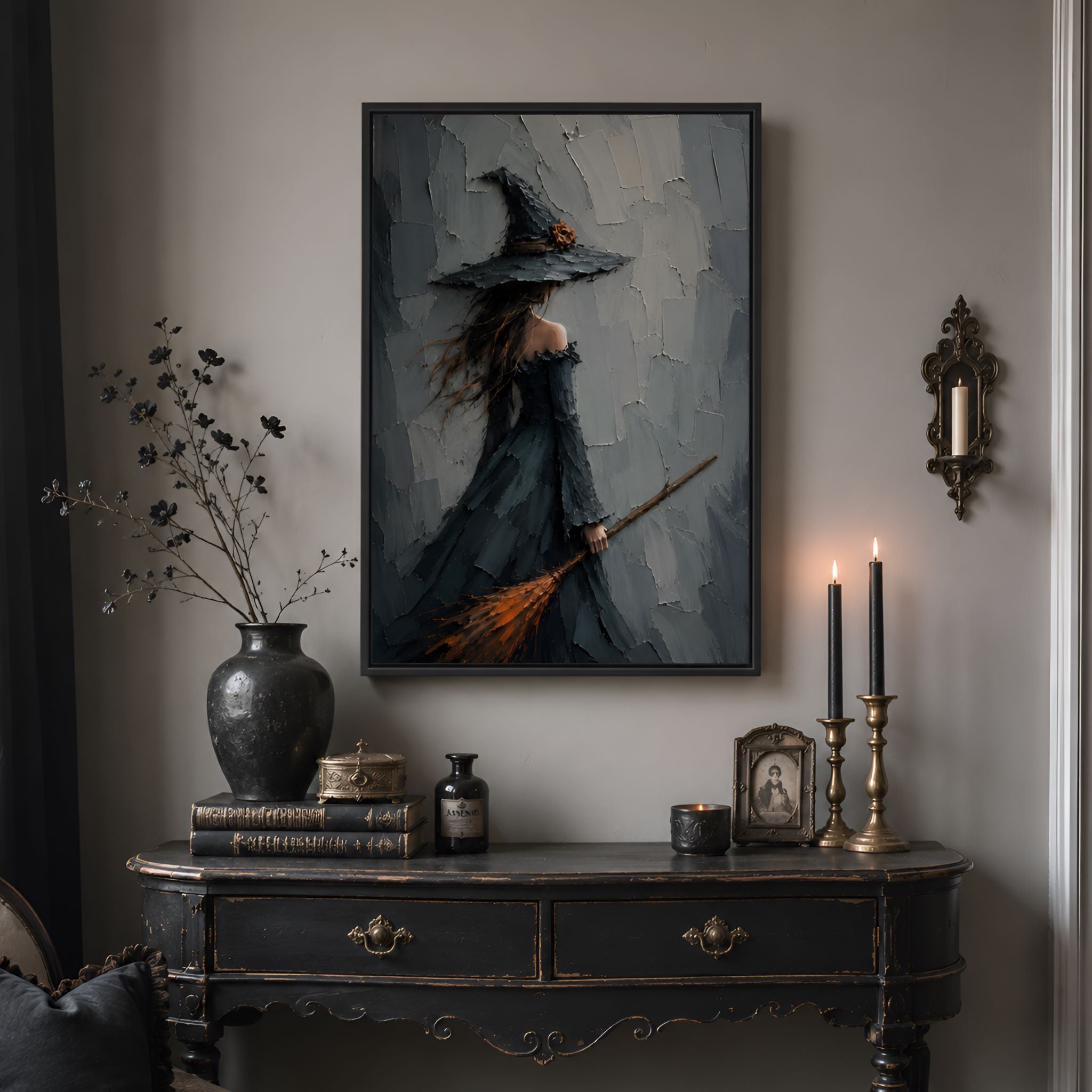 A whimsigoth living room with a witch-themed painting, candles, and books on a dark wooden table.