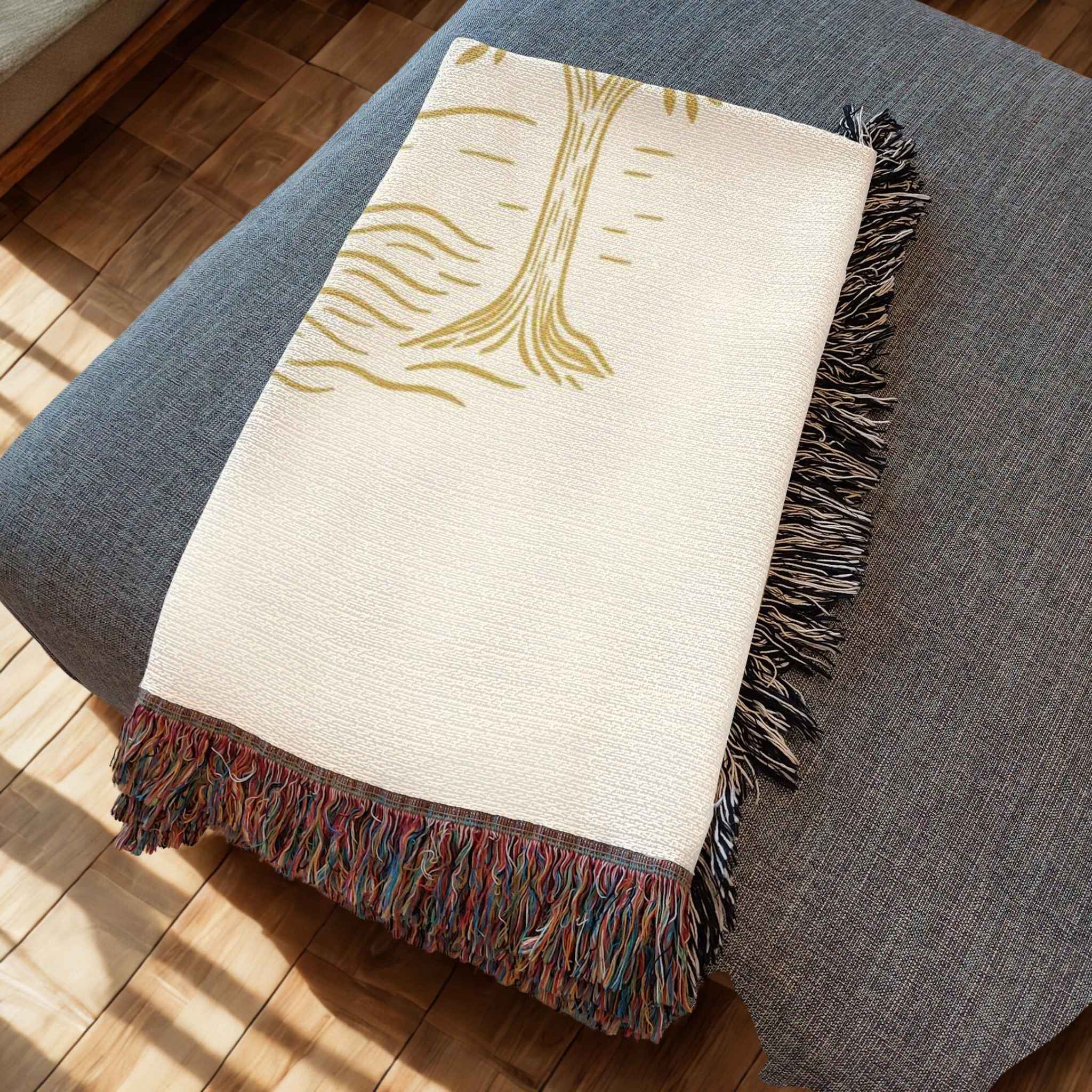 Beige blanket with gold tree design and colorful fringe on a gray surface.